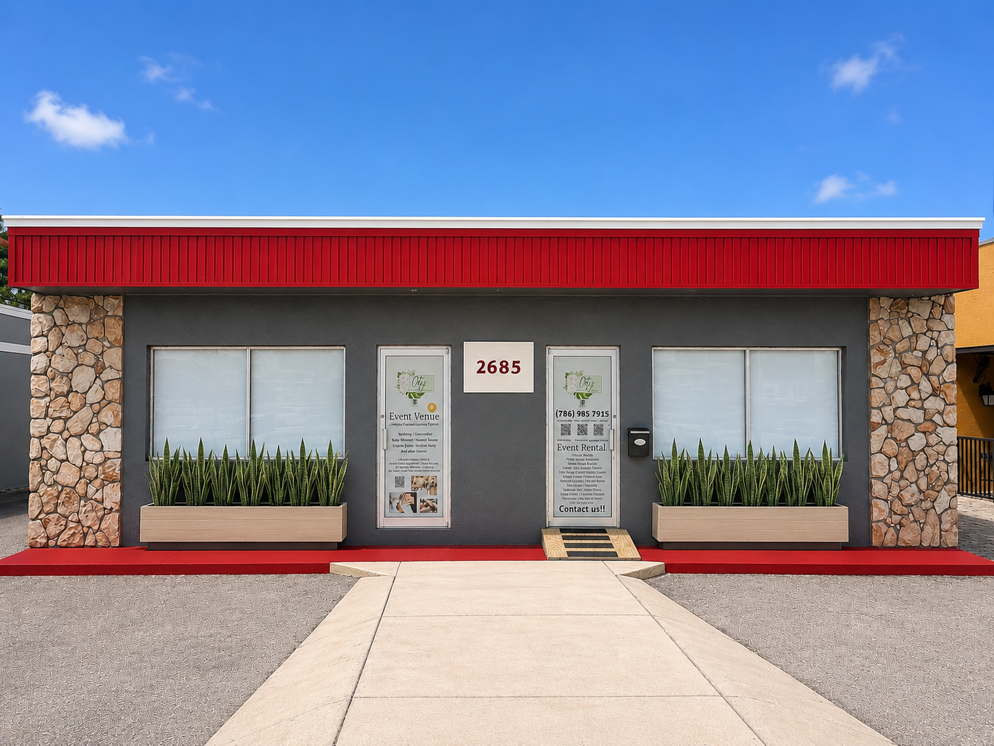 Front view of a commercial building with a dark gray facade, stone columns on each side, and red accents at the top and bottom. Large windows and doors display business signs for event venue and rental services. Green plants line the front on flower 