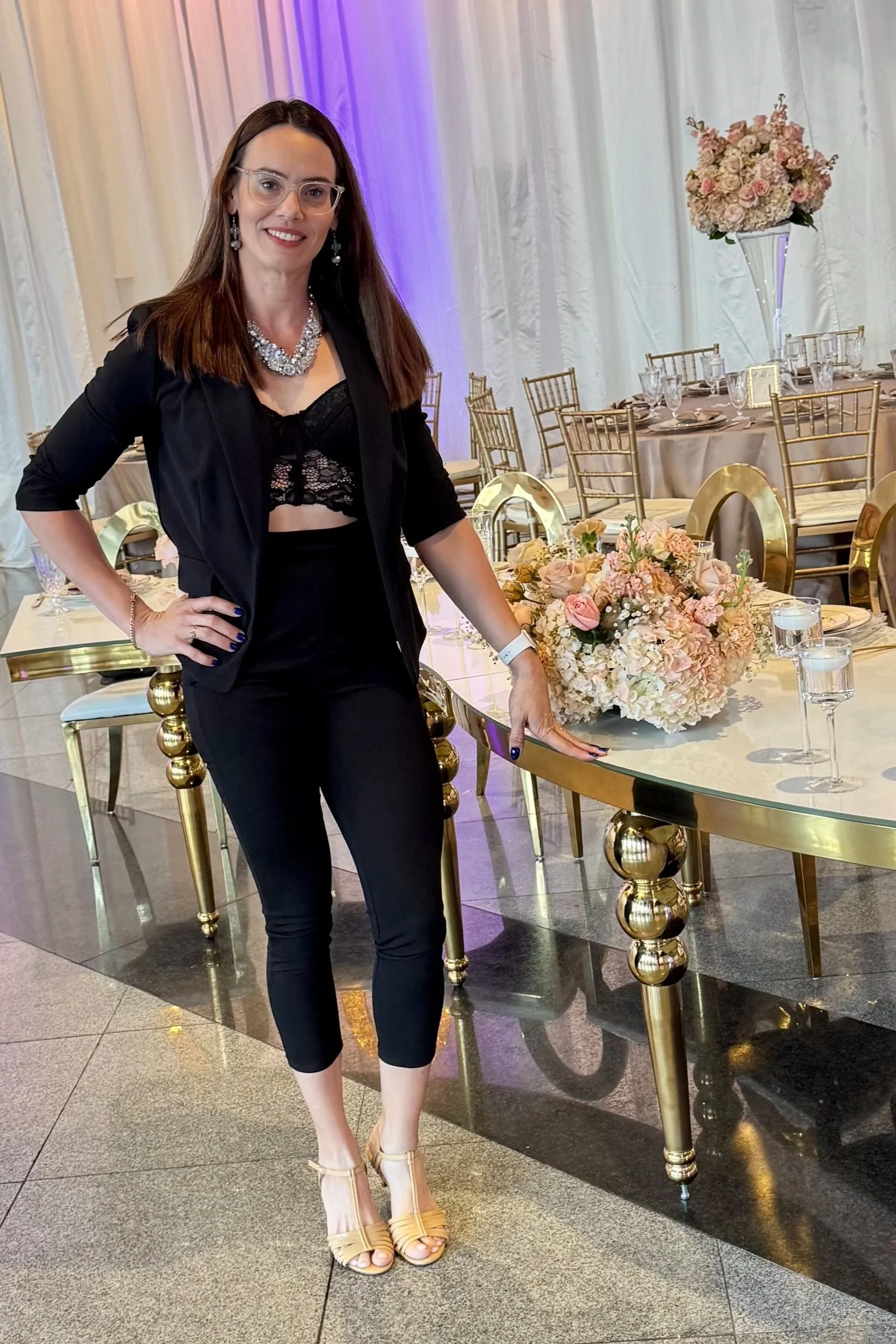 Woman dressed in black with a floral centerpiece table and wedding decor in the background.