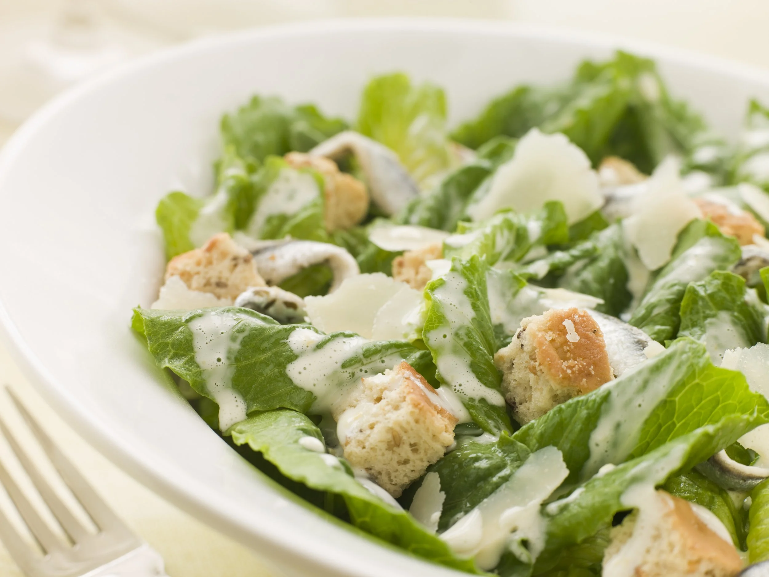 Caesar salad with romaine lettuce, croutons, shaved cheese, and creamy dressing in a white bowl.
