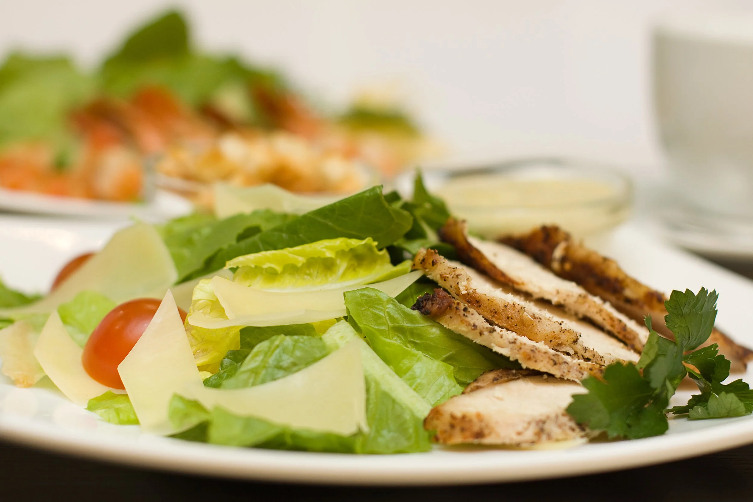 Fresh salad with grilled chicken, cherry tomatoes, lettuce, cheese, and herbs on a white plate.