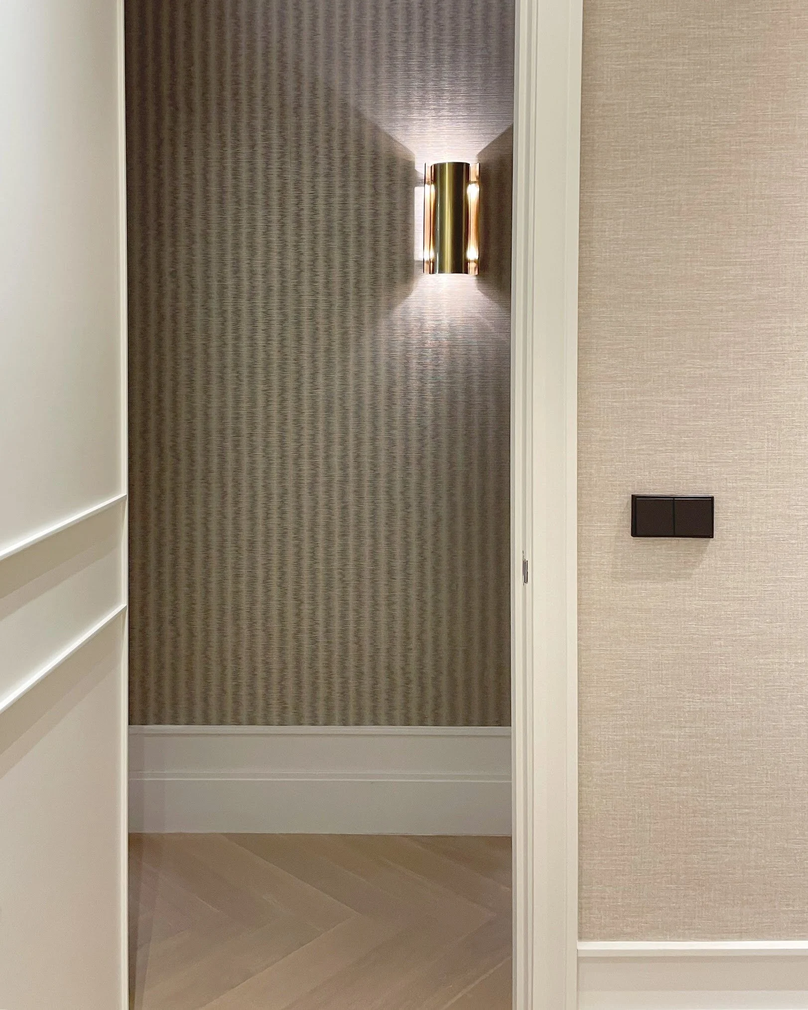 A hallway with textured wallpaper, a wall-mounted light fixture, and a beige carpet.