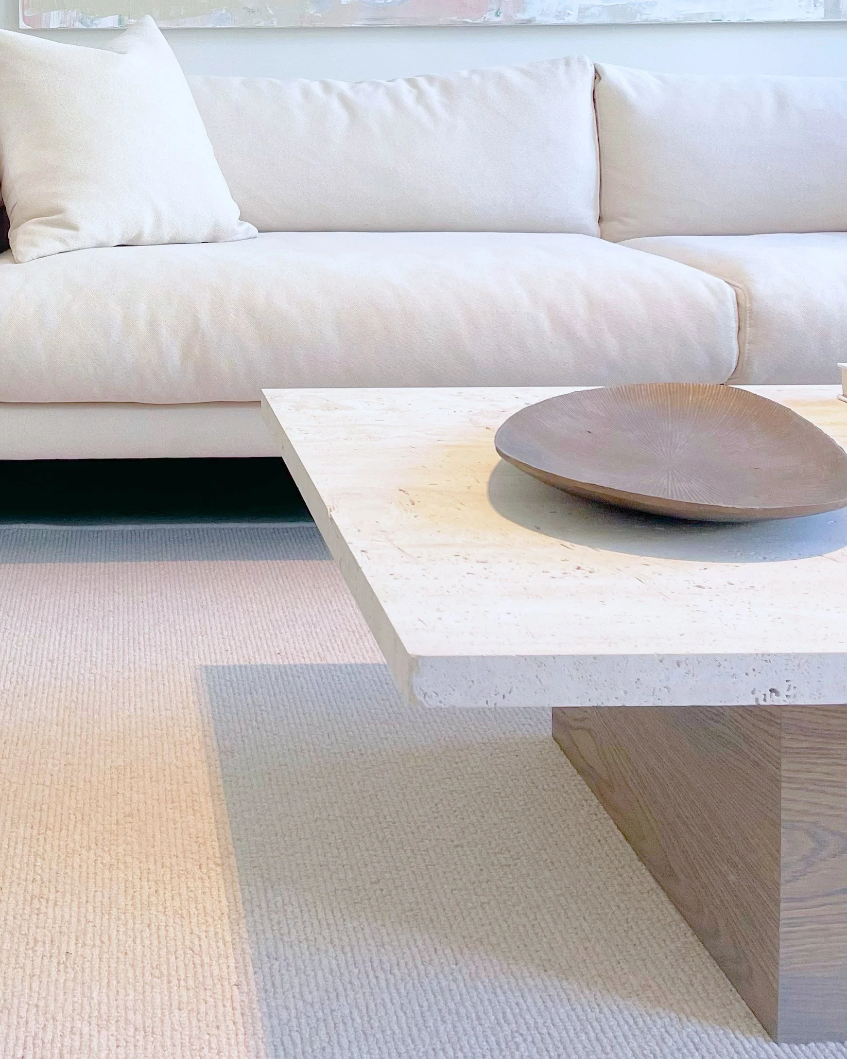 Close-up of a modern living room with a white sofa, a light-colored marble coffee table with a dark decorative bowl on top, and a beige area rug.