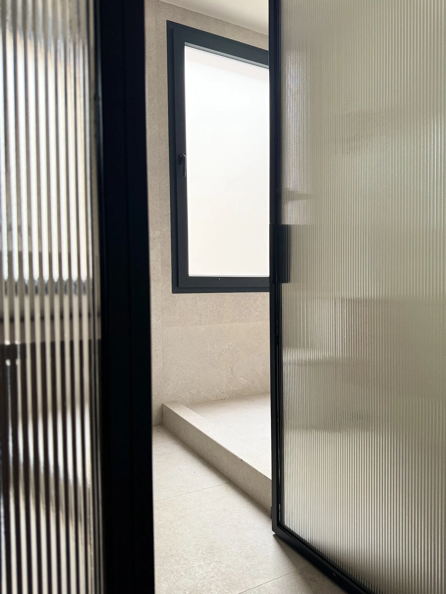 View of a minimalist modern space with a lattice-textured glass door, a frosted window, and a small step in a light-toned room.