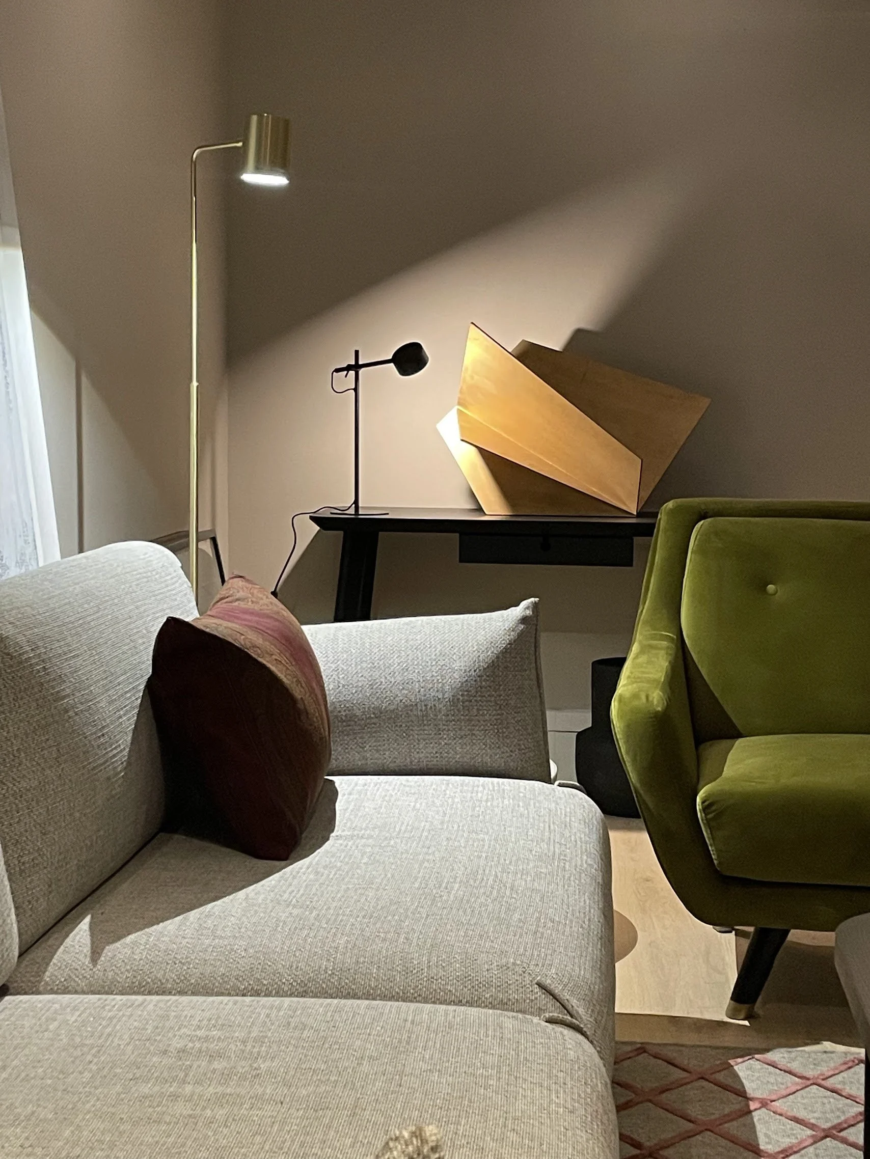 Living room with a beige sofa, a green chair, a side table with a unique wooden lamp, and two standing lamps—one tall gold and one black, in a cozy, modern setting.
