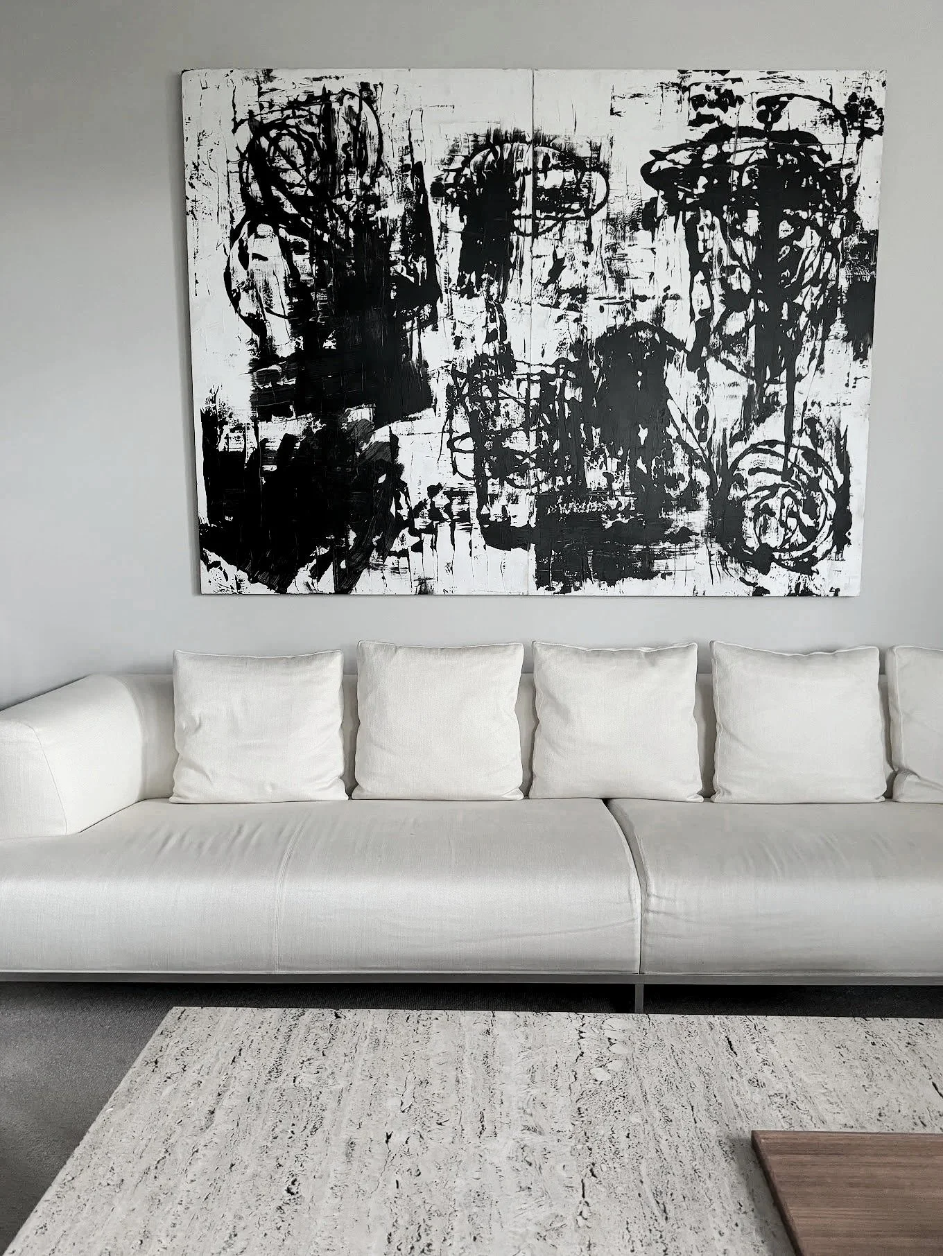 Modern living room with white sofa, multiple white pillows, abstract black and white artwork, and a white textured coffee table.