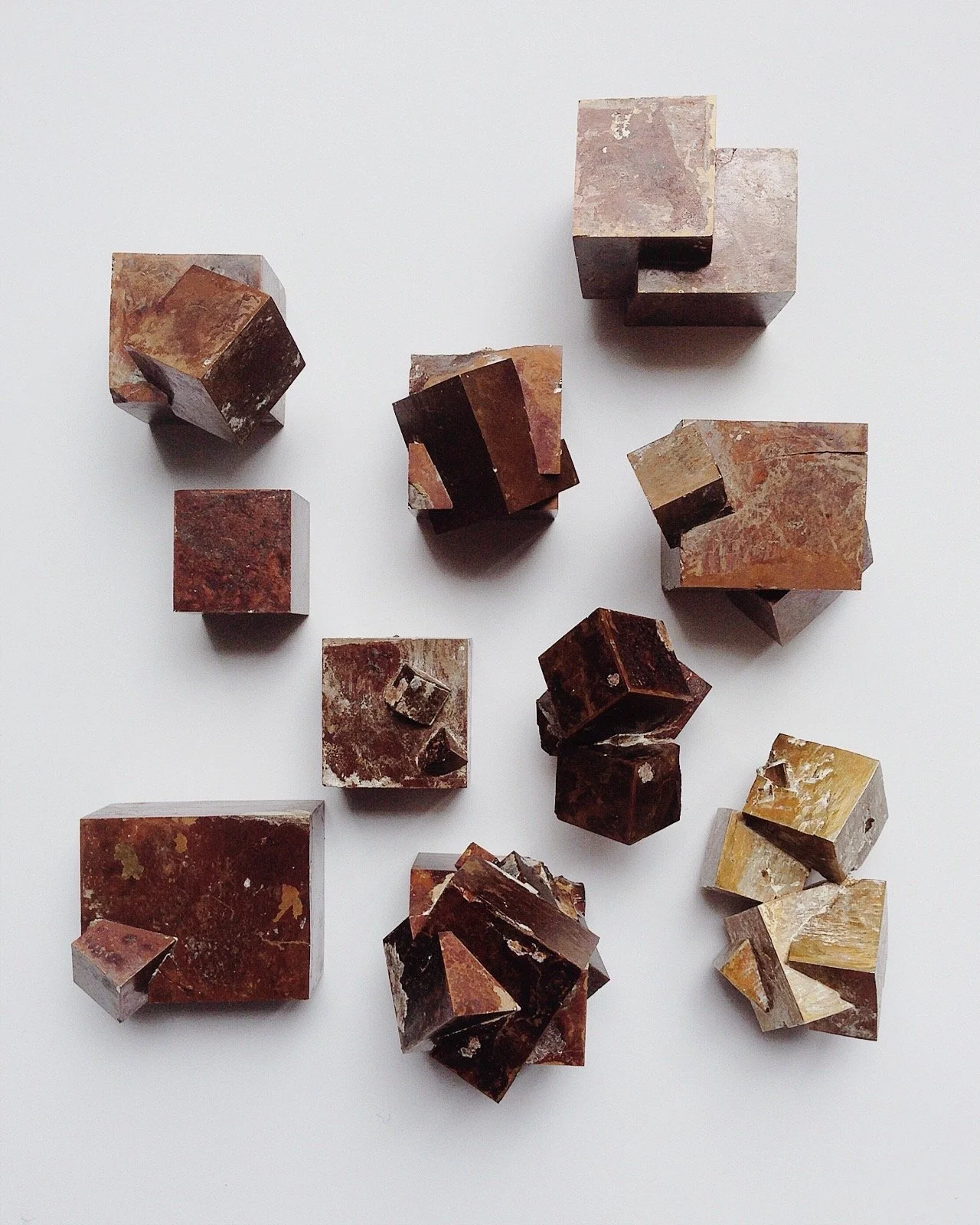 Several various-sized reddish-brown and tan stone or mineral cubes and blocks arranged on a white surface.