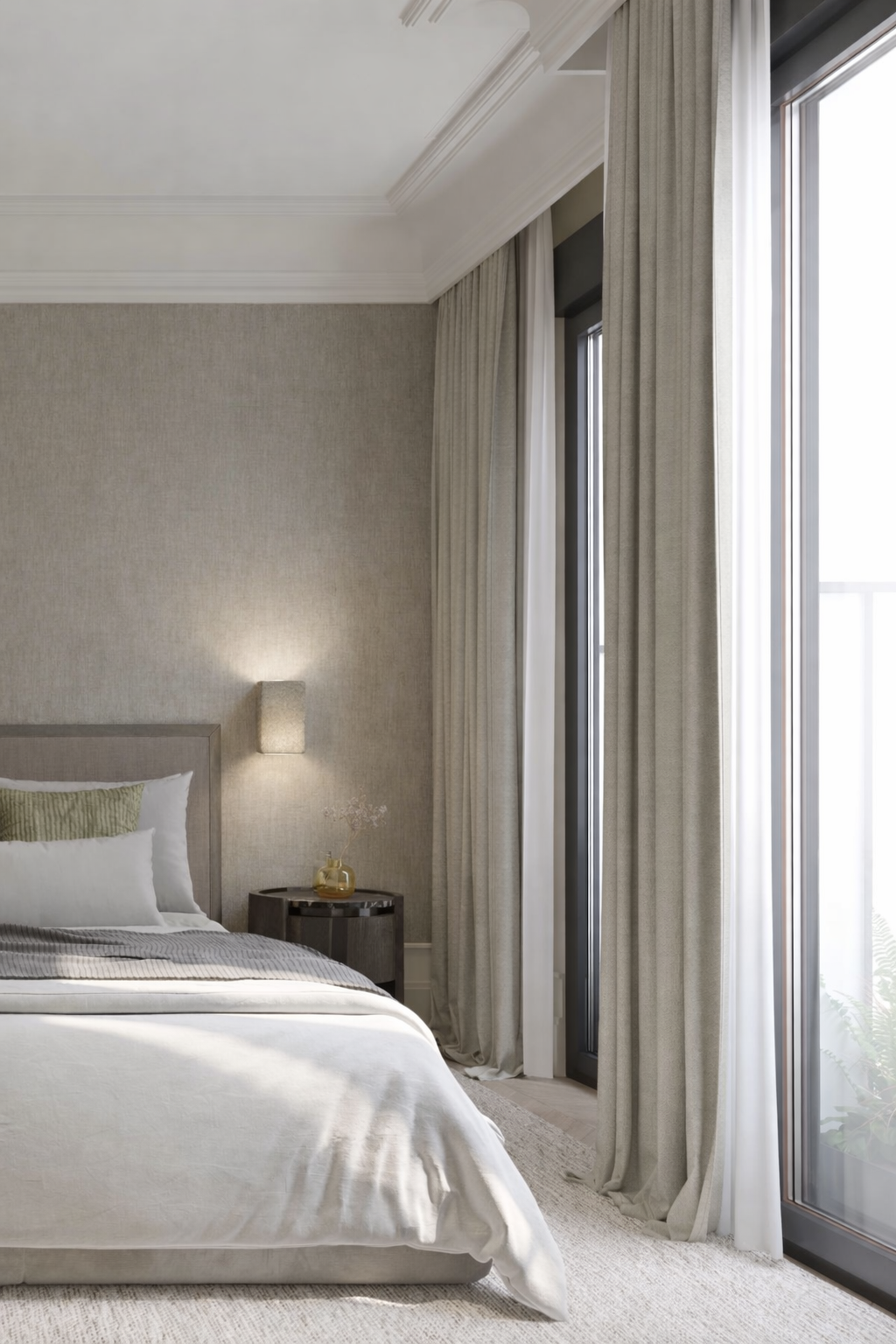 A cozy bedroom corner with a beige bed, pillows, a bedside table with a small vase, and large window with light-colored curtains.