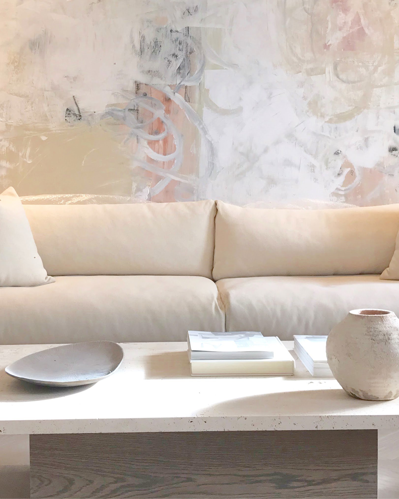 Modern living room with a beige sofa, abstract wall art, ceramic vase, and books on a white coffee table.