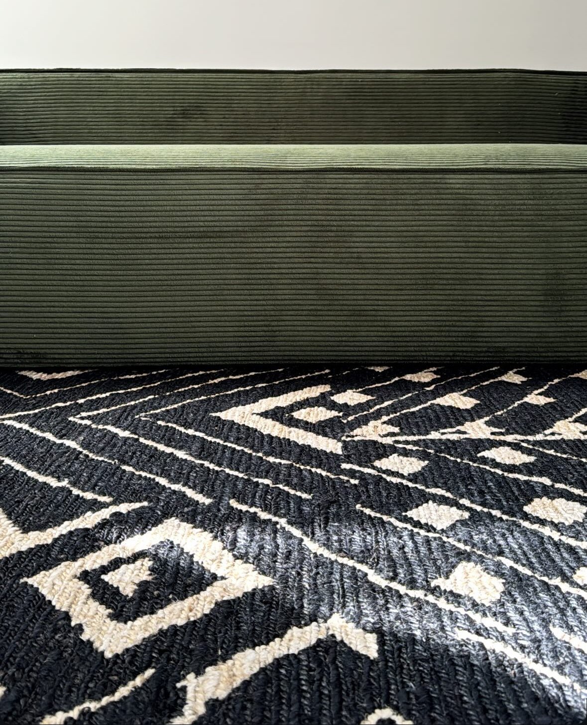 A dark green, textured storage ottoman placed on a black and white patterned rug.