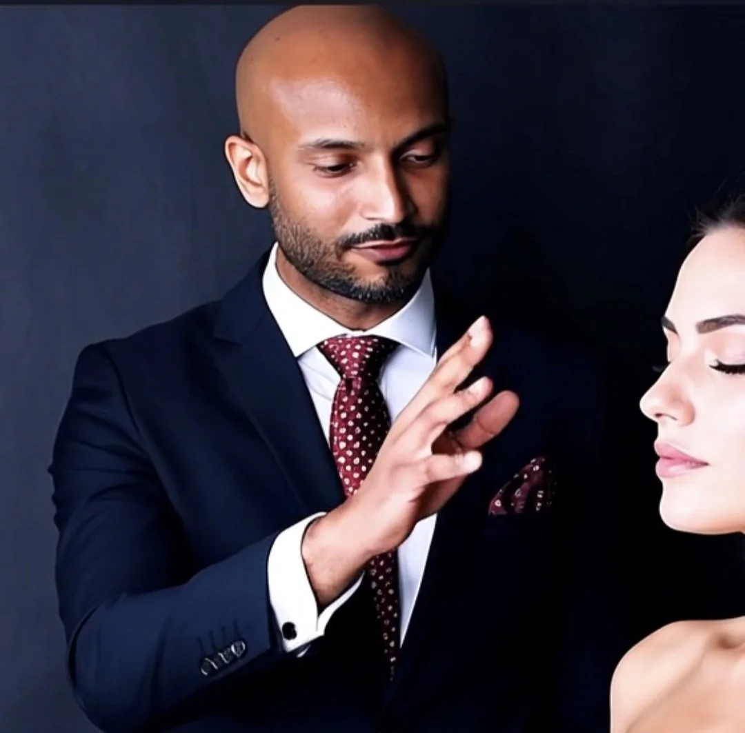 A man in a suit and a woman with closed eyes in front of him, with the man gently touching the woman's face.