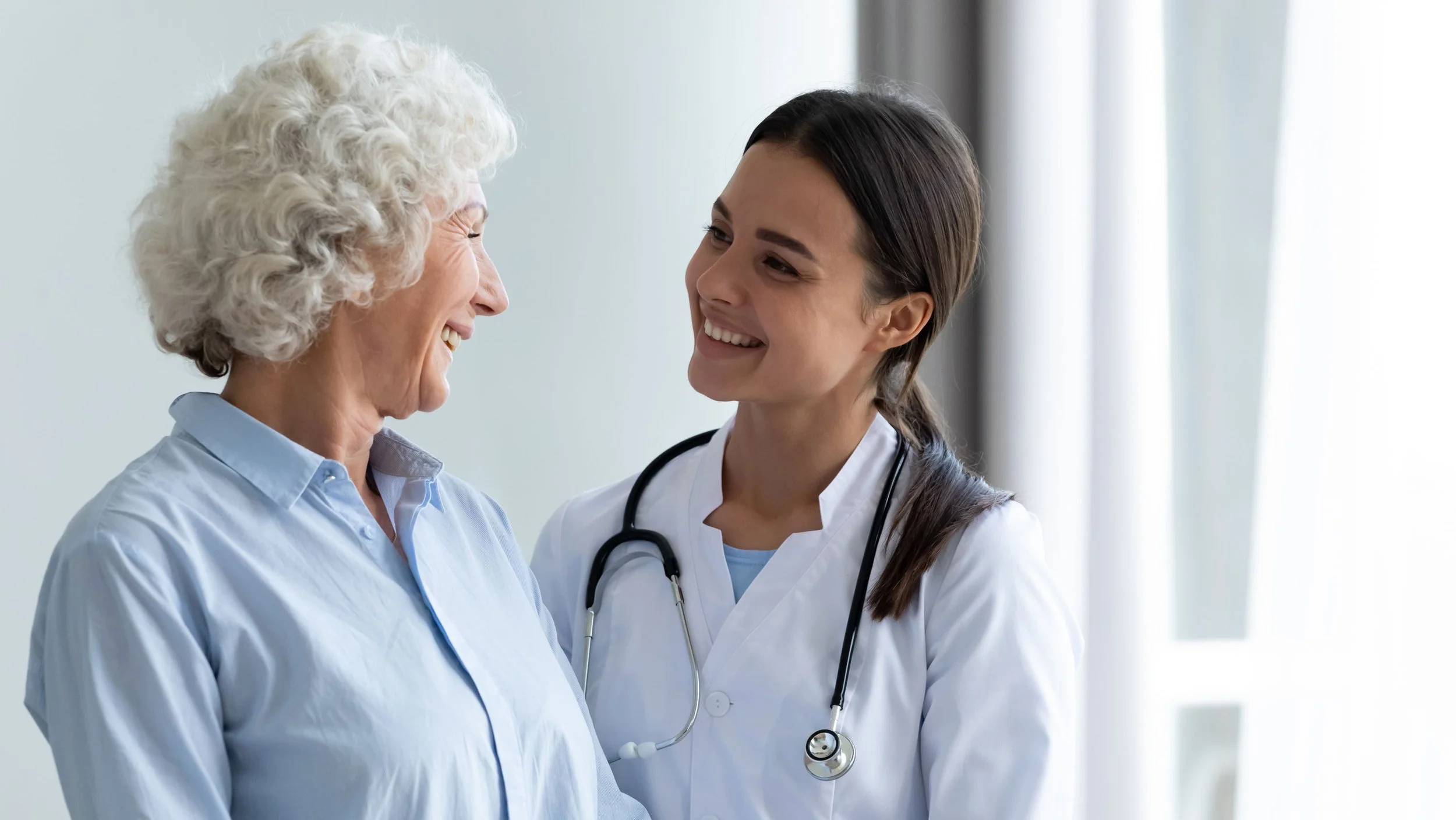 Woman in blue shirt smiling with a doctor in a white coat with brown hair
