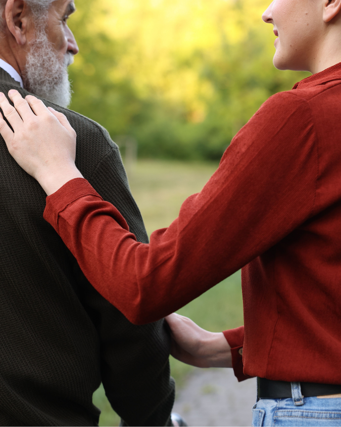 A woman gently touching an elderly man's shoulder outdoors during daytime.