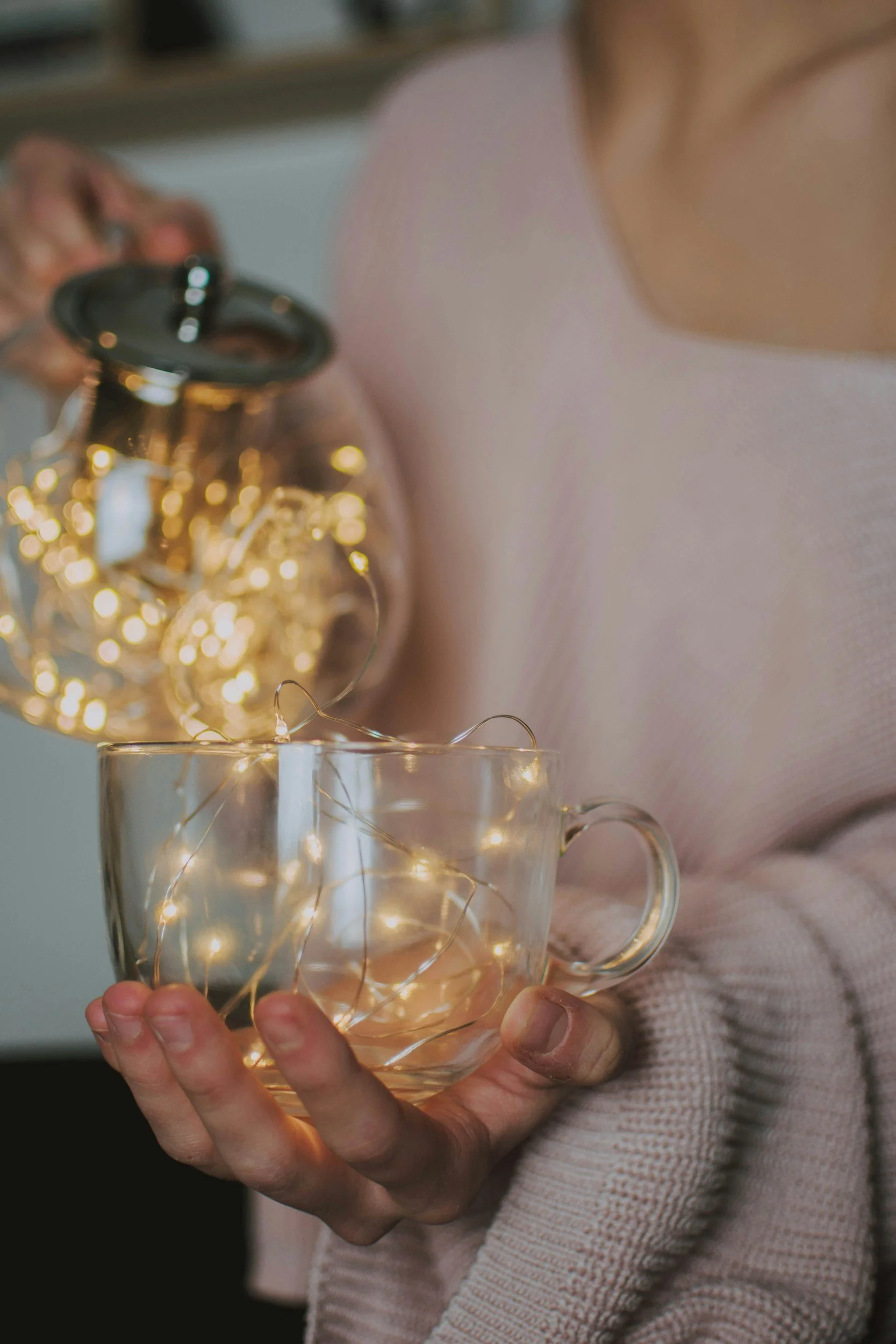 Person holding a glass mug with fairy lights inside, while pouring a glass jar filled with fairy lights.
