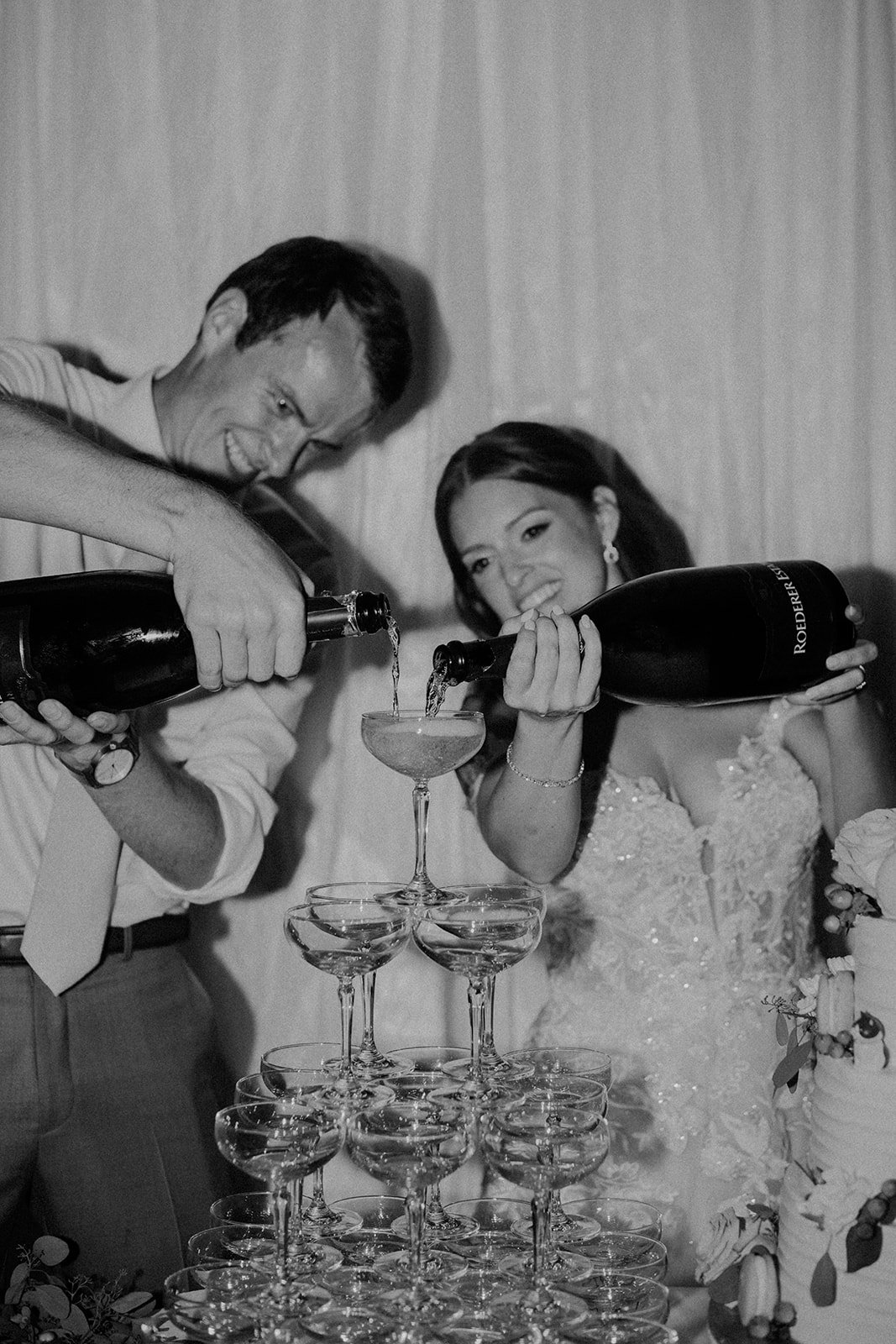 A couple at a wedding celebration pouring champagne into a pyramid of glasses.