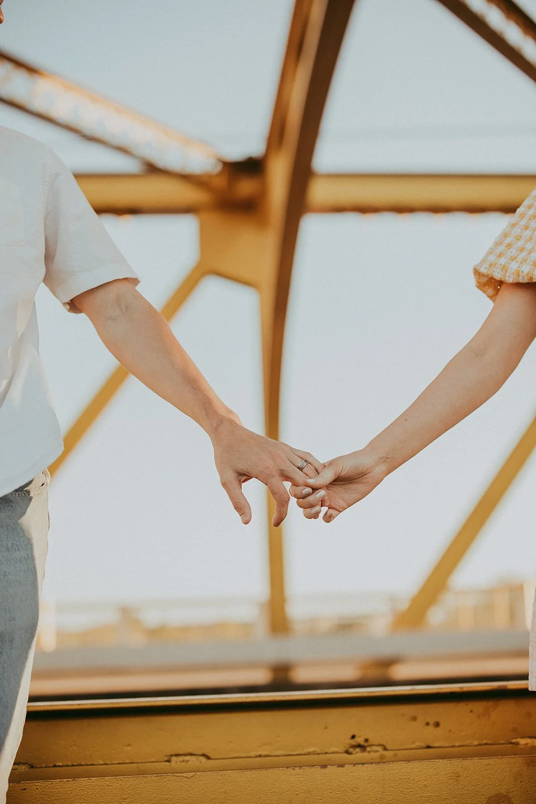 A man and woman holding hands, with the man's hand on the left and woman on the right, under a wooden pergola or trellis.