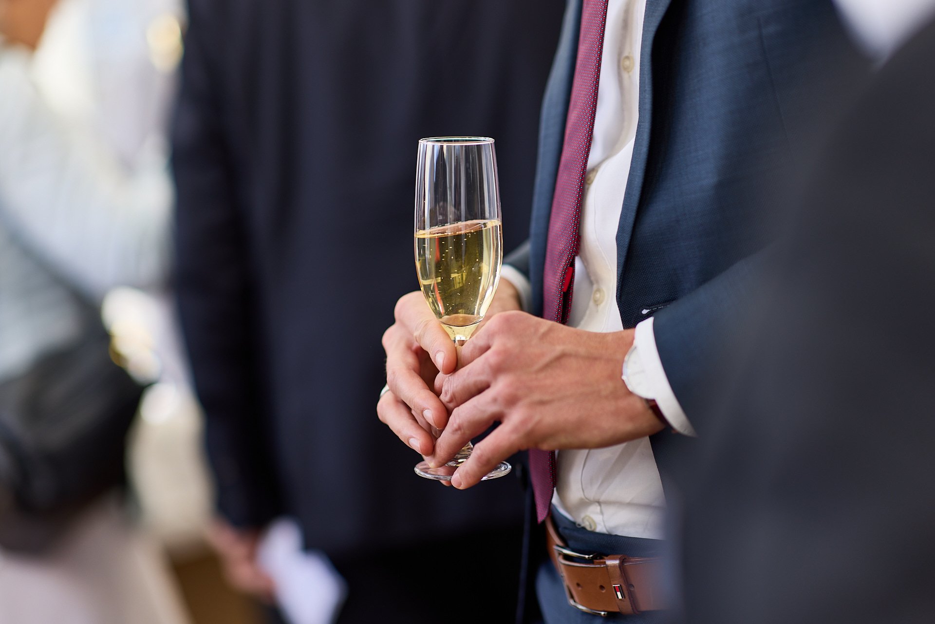 Person hält ein Glas Champagner bei einer Feier im formellen Anzug.
