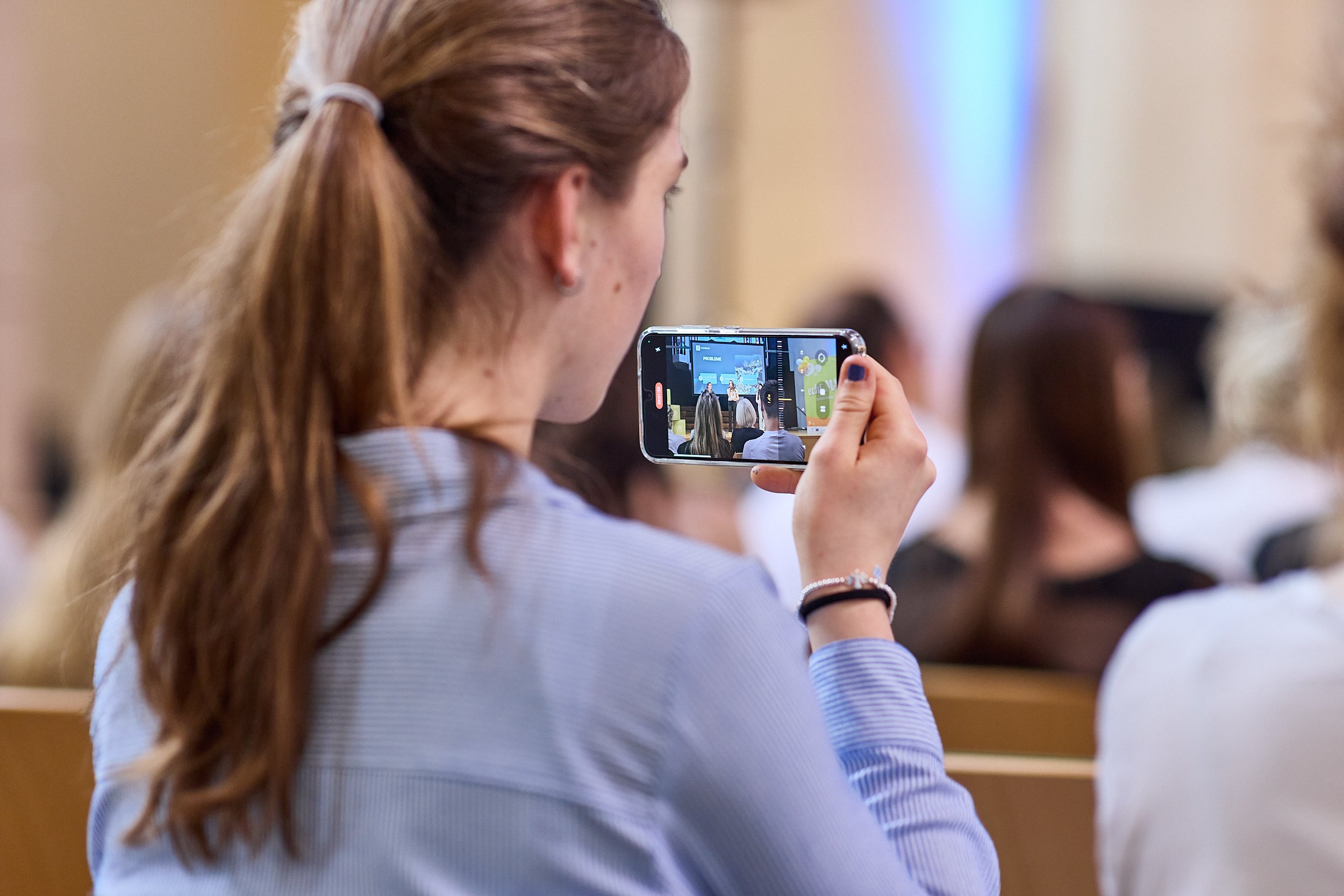 Frau nimmt ein Foto oder Video von einem Vortrag oder eine Präsentation auf einem Smartphone in einem Auditorium auf.