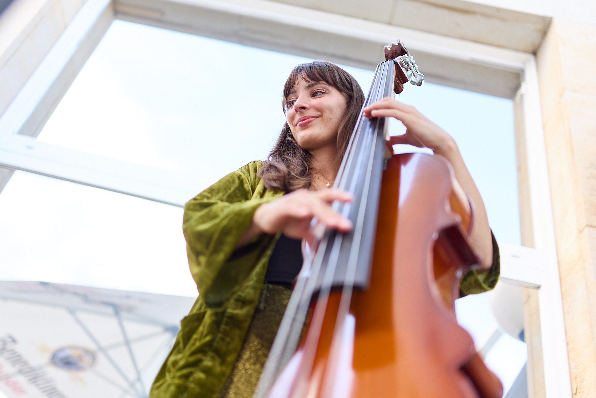 Junge Frau spielt Gitarre auf einer Terrasse im Freien, lächelt.