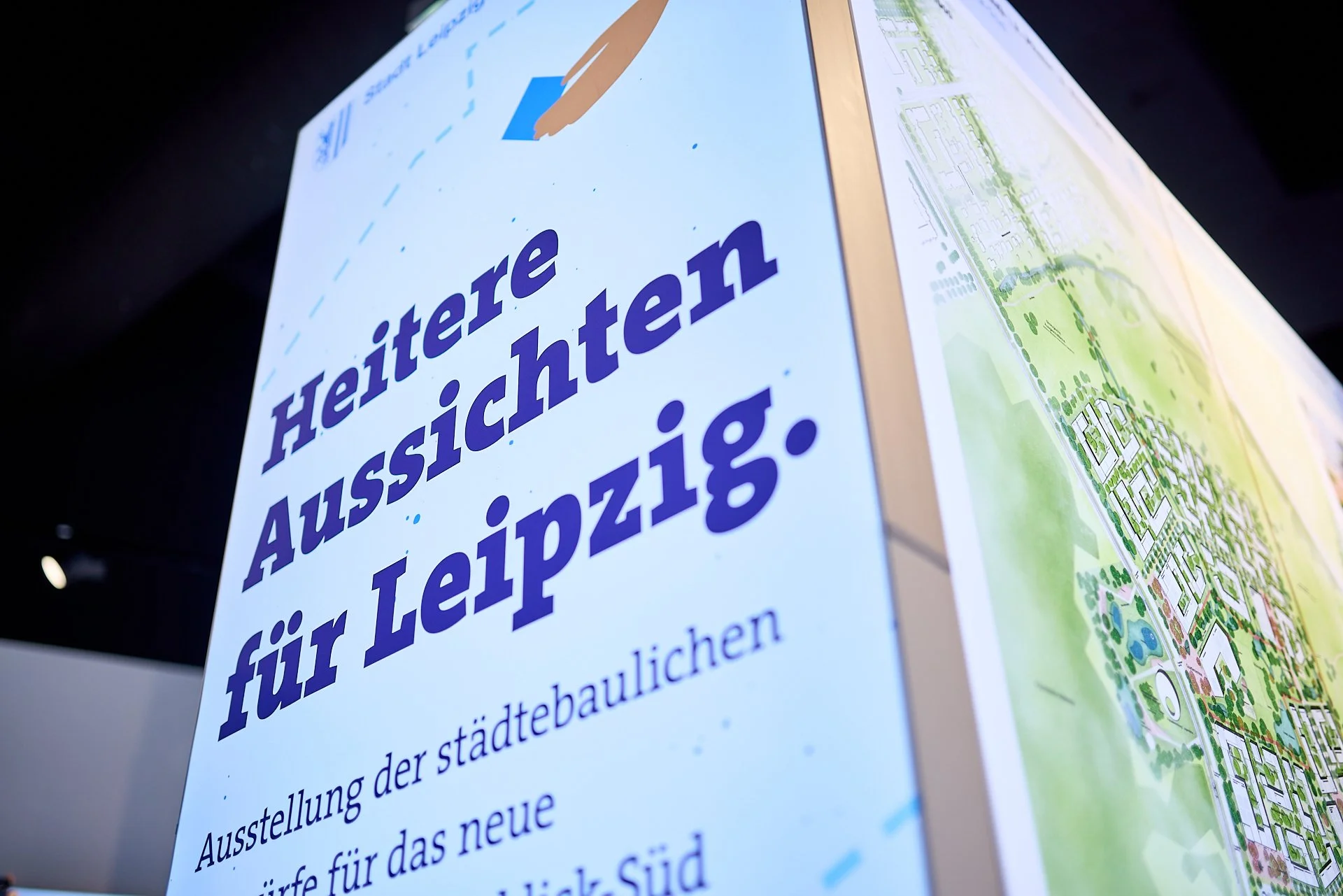 Schild mit Text auf Deutsch, das auf eine Ausstellung über Stadtentwicklung in Leipzig hinweist, mit grafischem Stadtplan im Hintergrund.