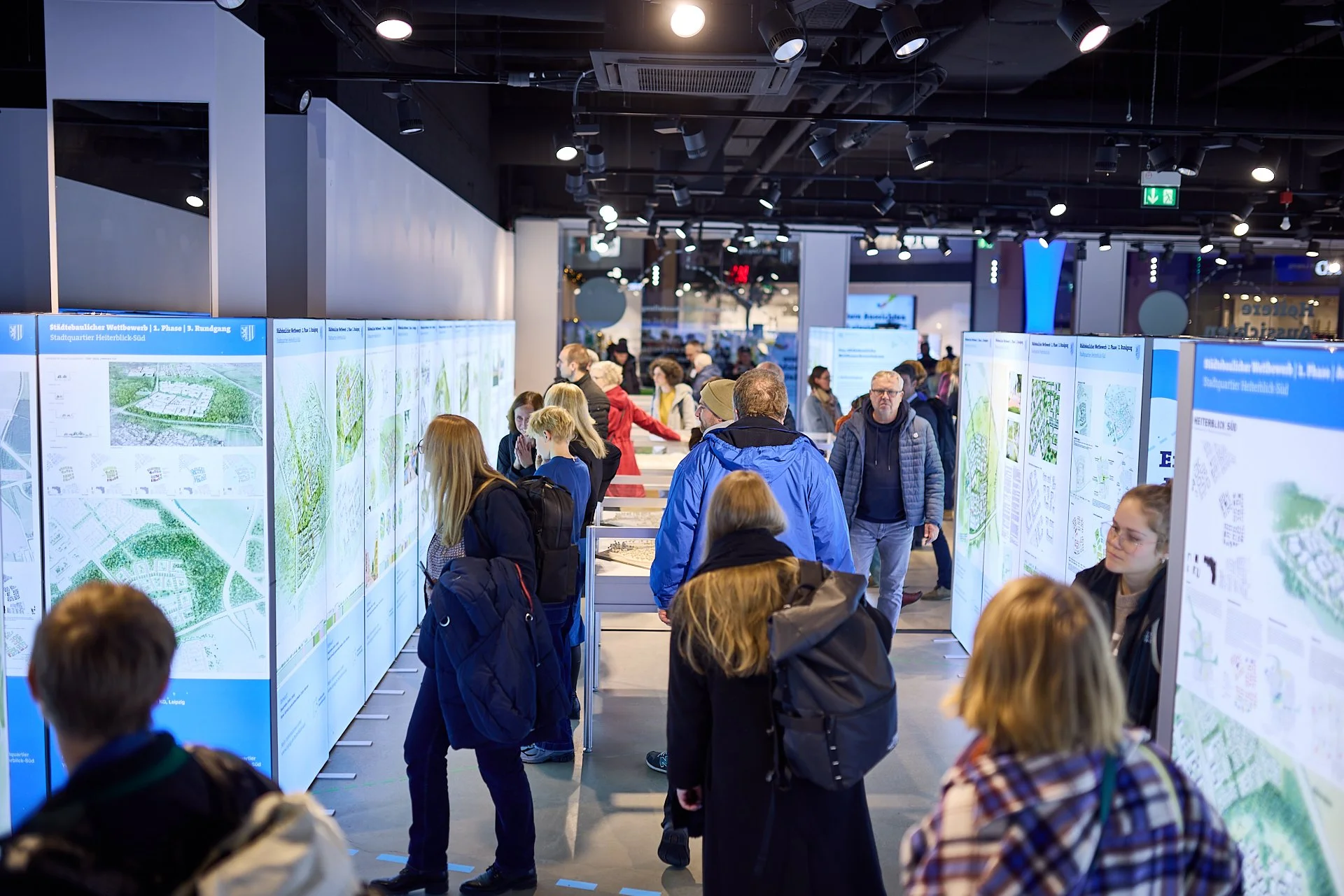 Menschen betrachten Pläne und Karten bei einer Ausstellung in einem modernen Ausstellungsraum.