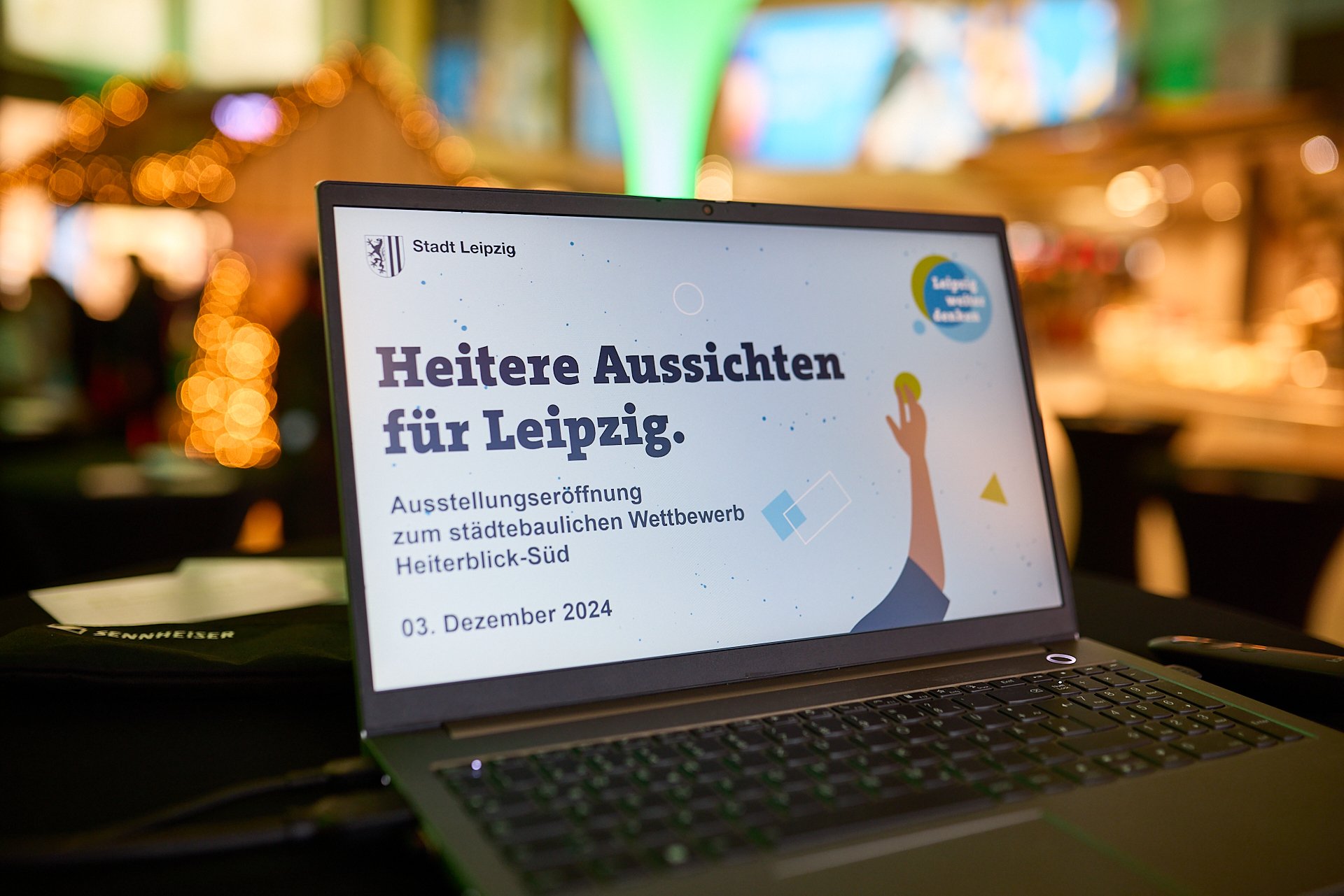 Laptop-Display zeigt Ankündigung der Eröffnung einer Ausstellung in Leipzig am 3. Dezember 2024, im Rahmen eines städtebaulichen Wettbewerbs, mit dem Titel 'Heitere Aussichten für Leipzig'.