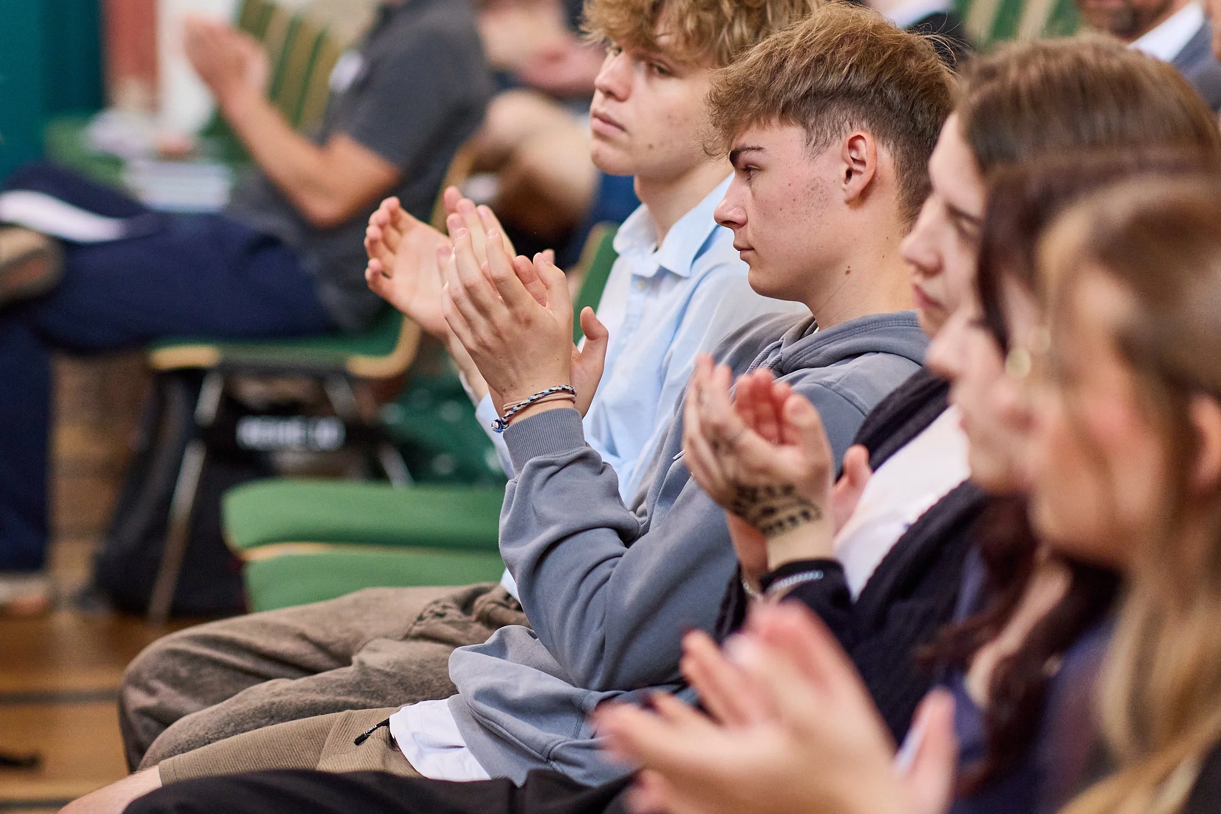 Junge Menschen sitzen in einem Raum und applaudieren bei einer Veranstaltung.
