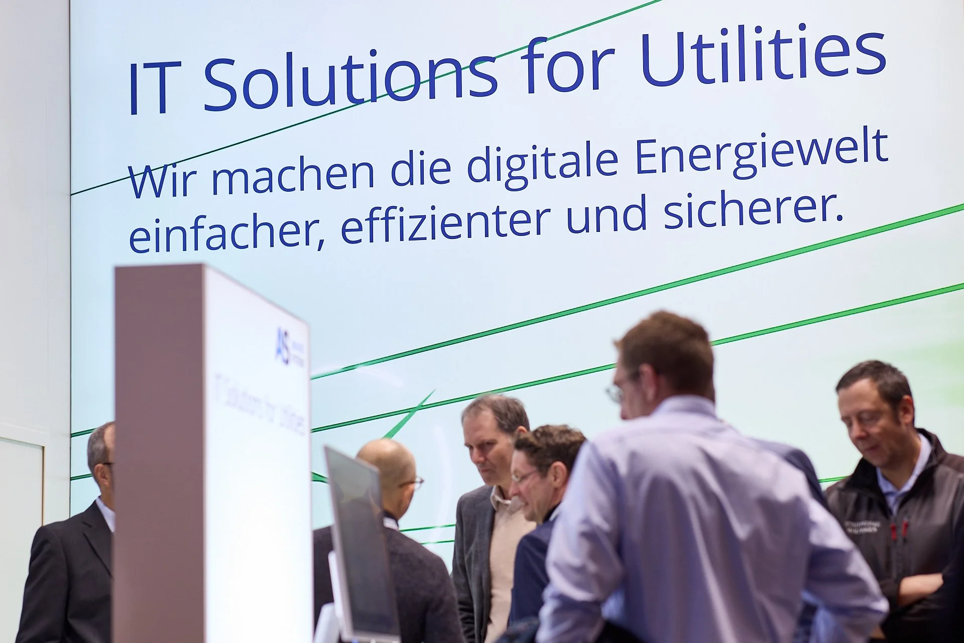 Menschen versammeln sich vor einem großen Bildschirm bei einer IT-Messe, der die Botschaft zeigt: 'IT Solutions for Utilities'.