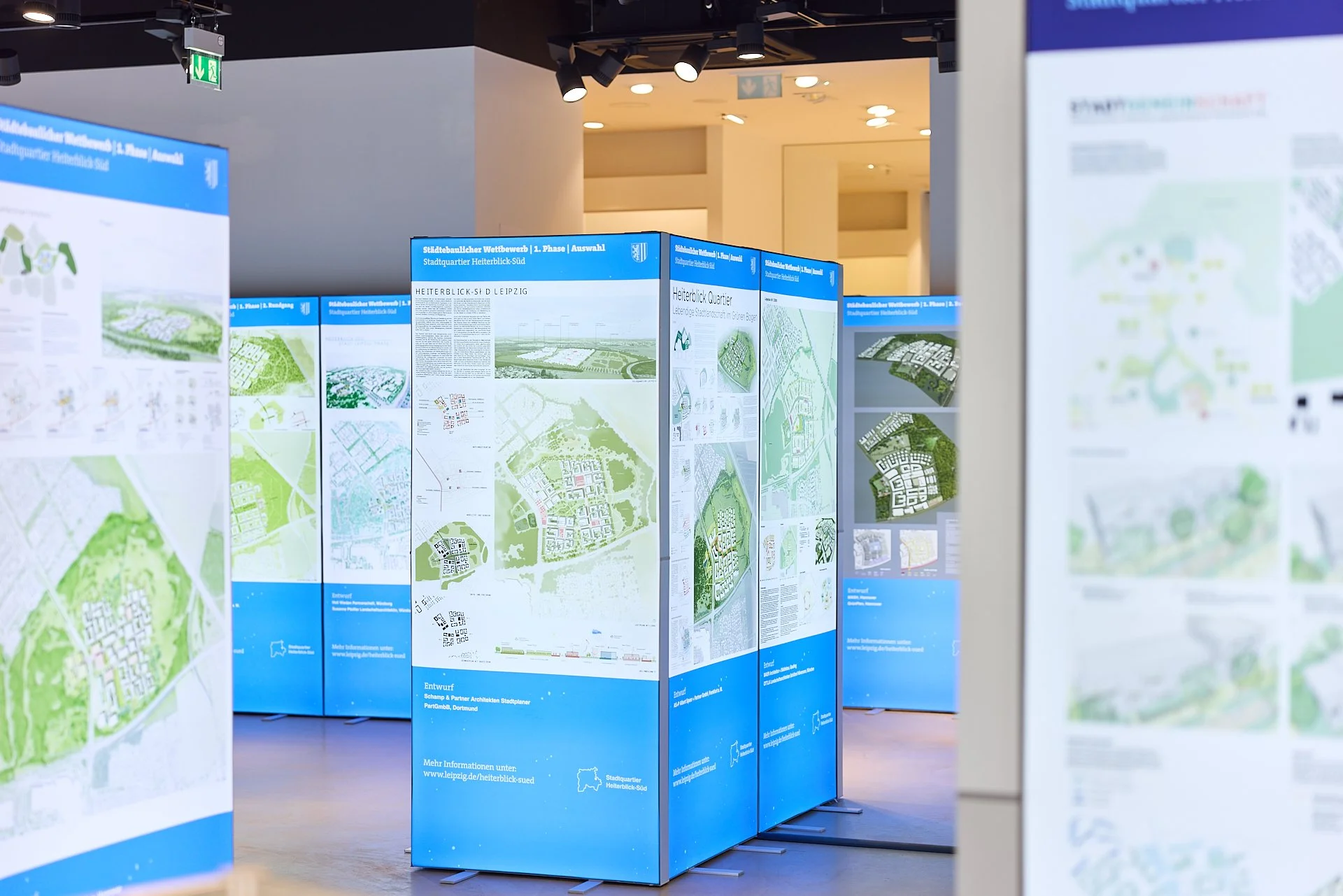 Mehrere blaue Stellwände mit Stadtplänen und Plänen für ein städtebauliches Projekt in einem Ausstellungsraum.