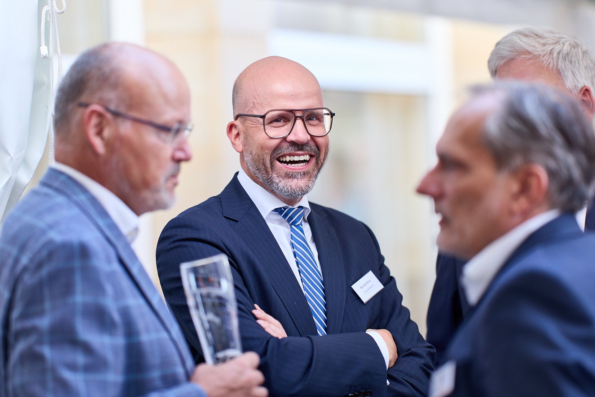 Männer im Businessoutfit im Gespräch bei einer Konferenz, eines lächelt freundlich in die Kamera.