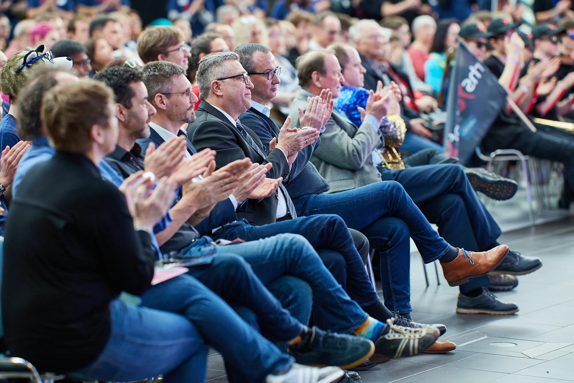 Menschen sitzen in einem Saal und applaudieren bei einer Veranstaltung.