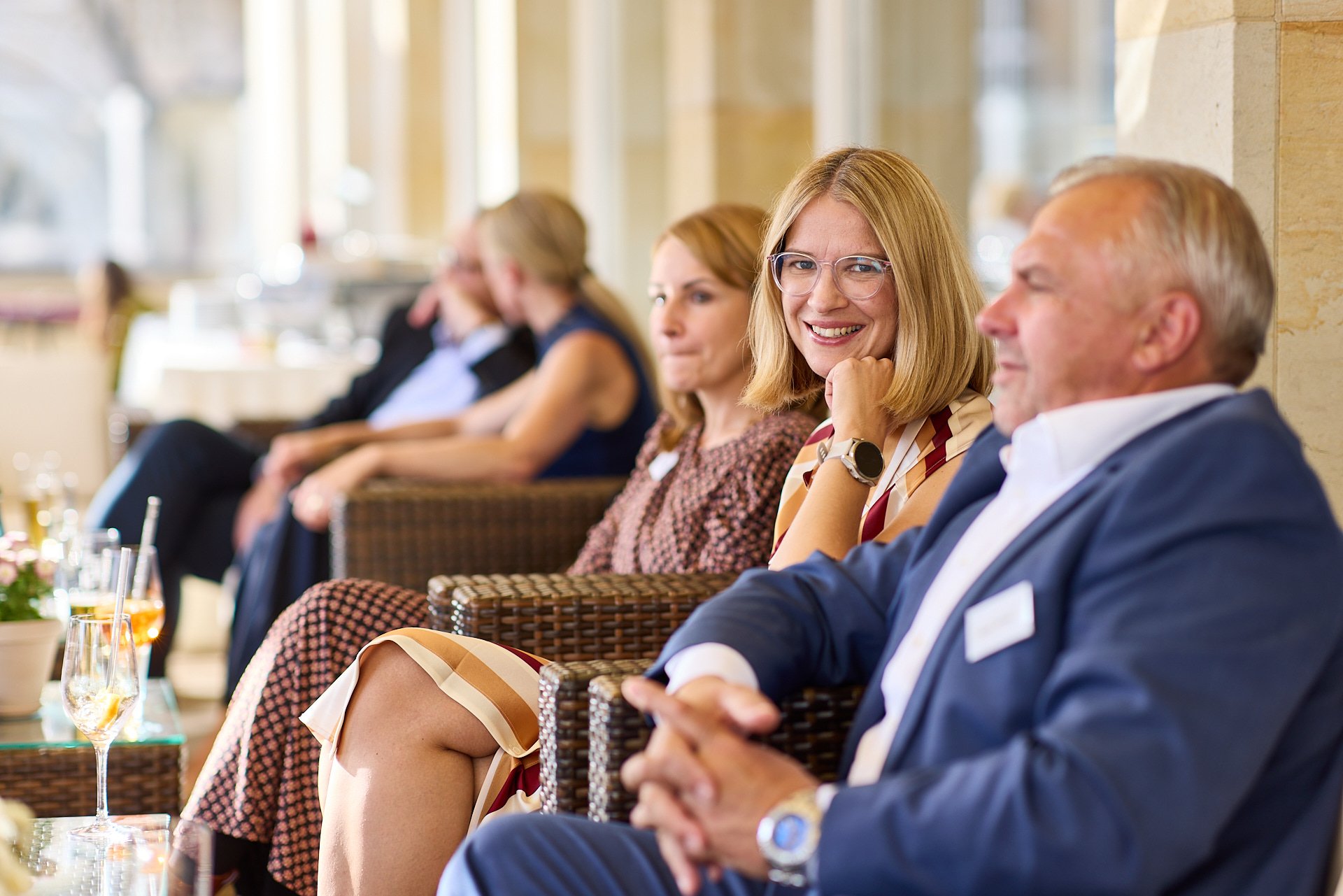Menschen sitzen in einer Lounge und unterhalten sich, während sie an einem Event oder einer Konferenz teilnehmen, mit einem Blick auf freundliche Atmosphäre.