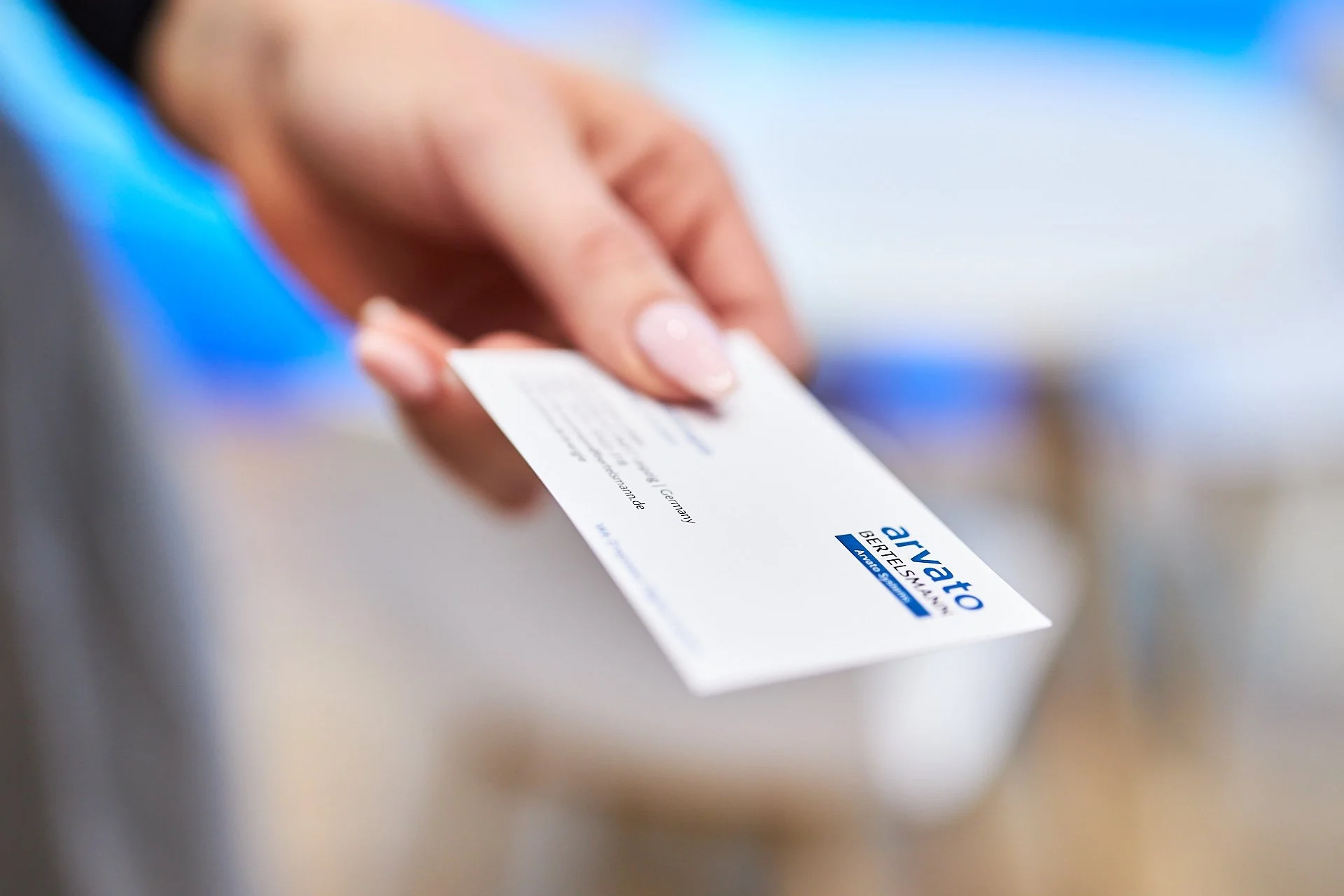 Hand hält eine Arvato Karte mit blauer und schwarzer Schrift auf weißem Hintergrund.