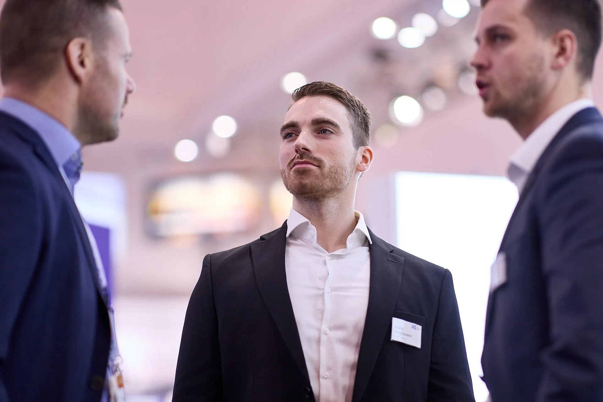 Drei Männer in formeller Kleidung sprechen auf einer Konferenz oder einem beruflichen Event.