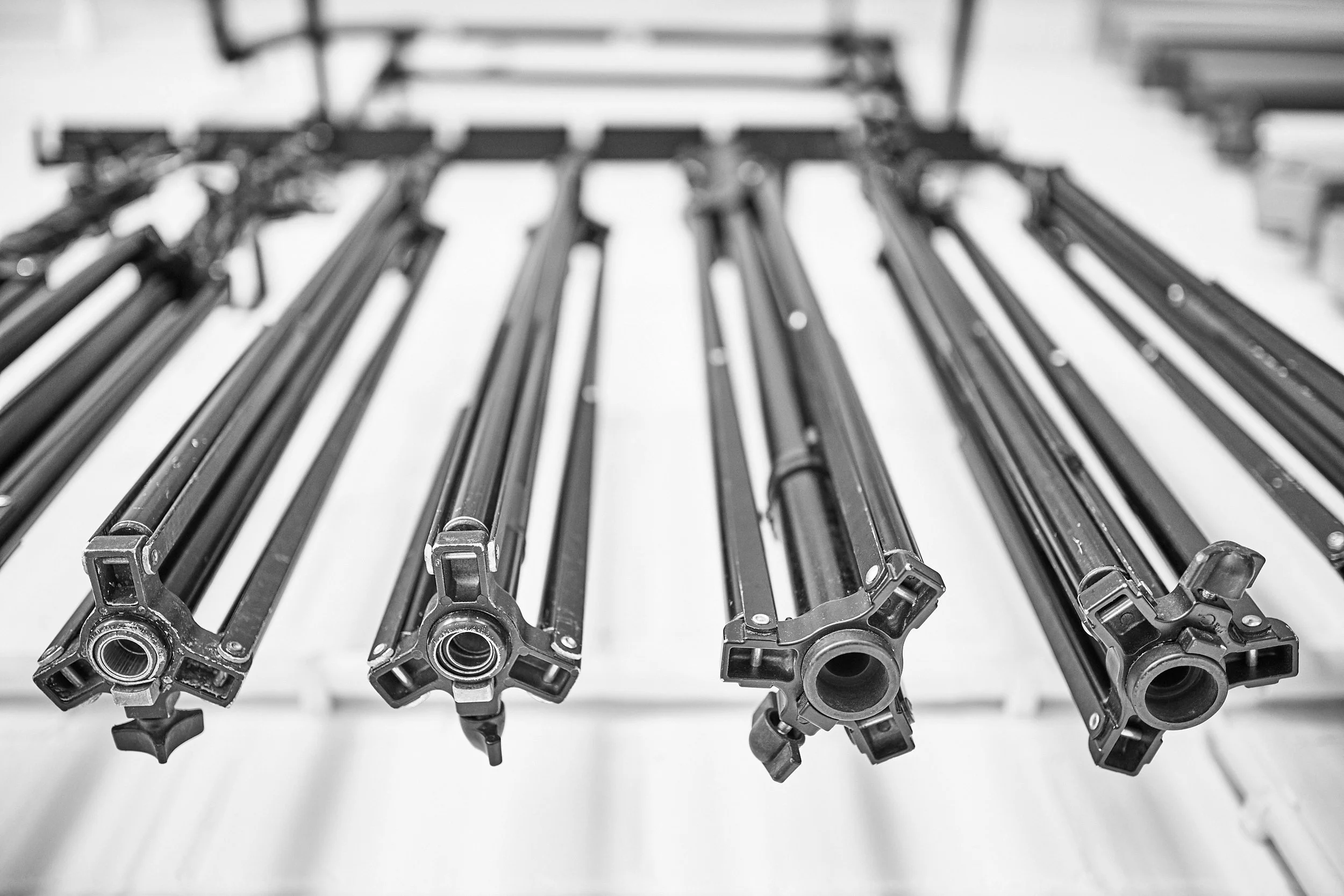 Blick auf mehrere Aluminiumstranglen für fotografische Stative, die auf einer weißen Oberfläche liegen.