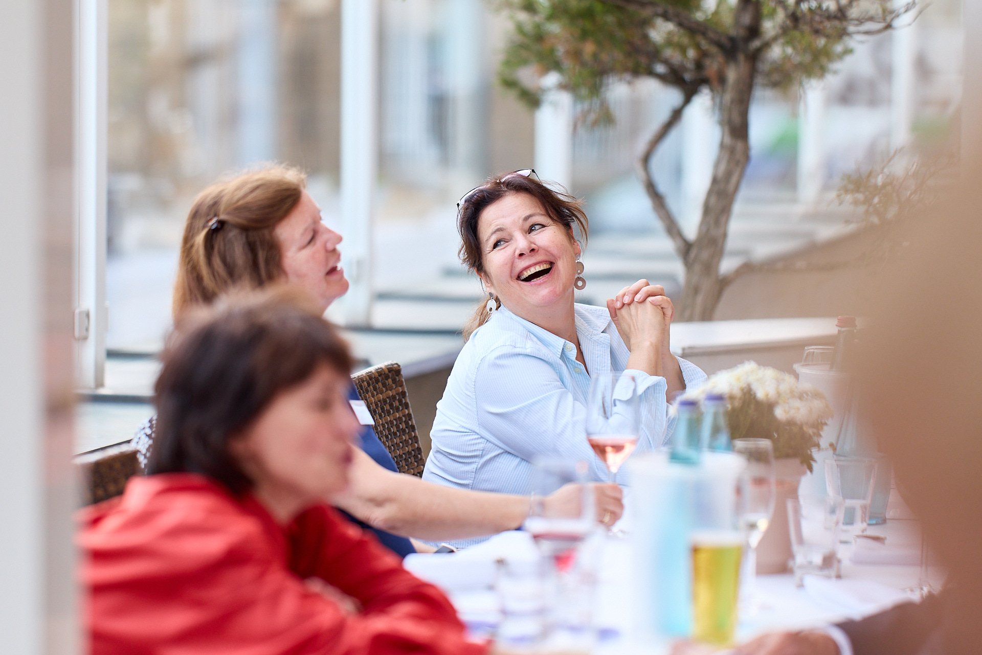 Drei Frauen sitzen an einem Tisch in einem hell erleuchteten Raum, lachen und unterhalten sich.