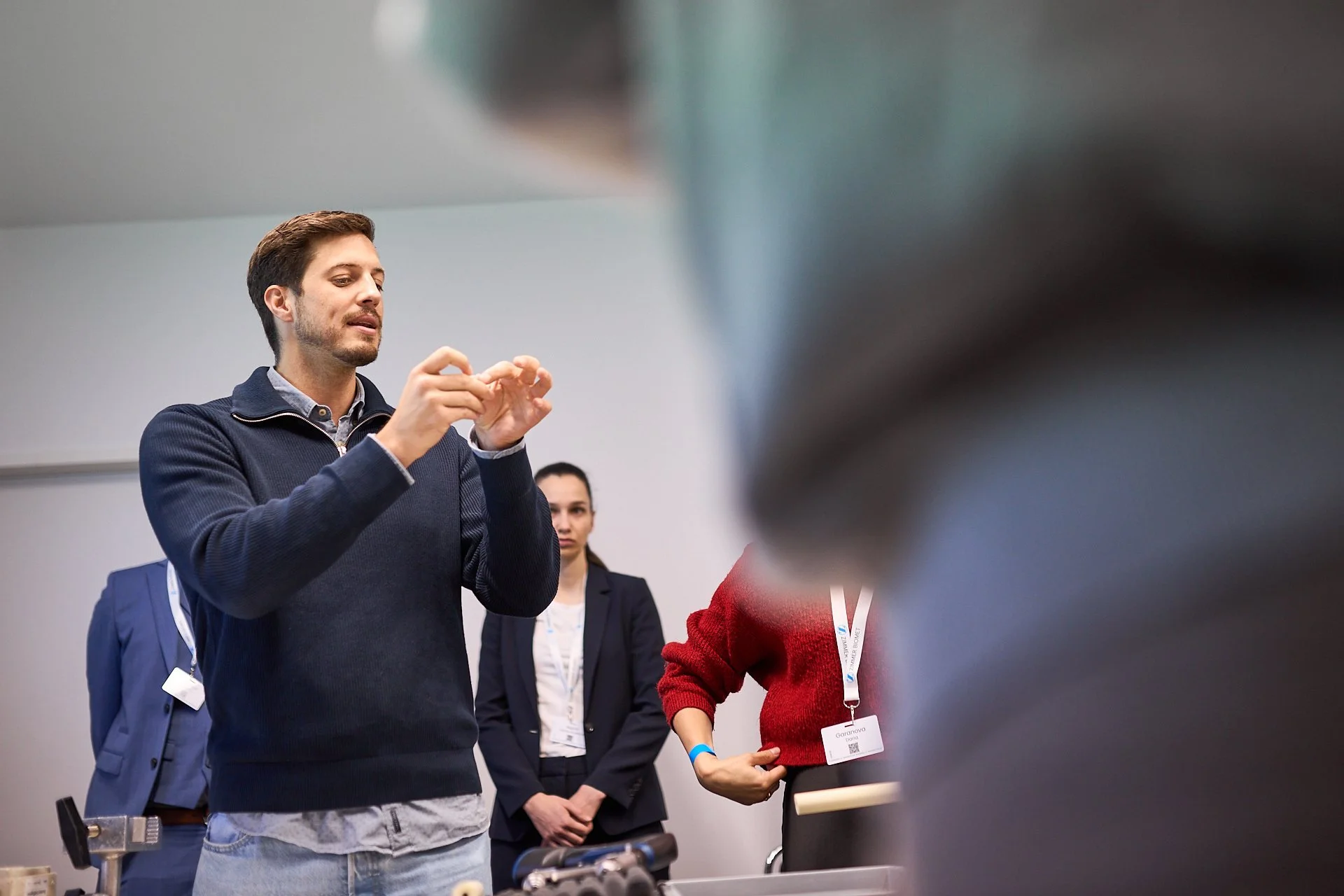 Ein junger Mann erklärt etwas vor einer Gruppe von Menschen bei einer Präsentation oder Demonstration in einem Konferenzraum.