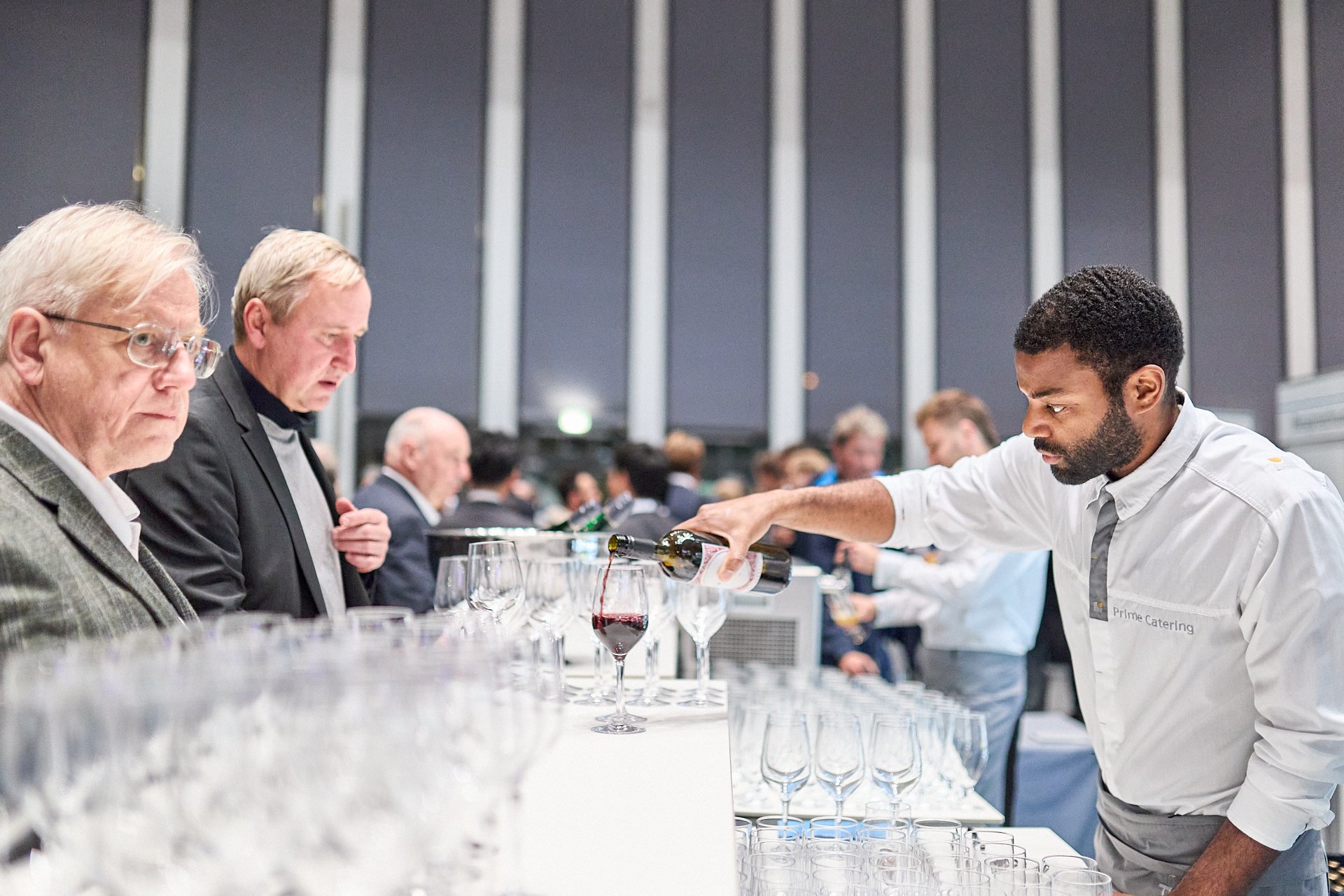 Mann beim Weinverkostung im Trinklabor, während weitere Personen im Hintergrund sitzen.