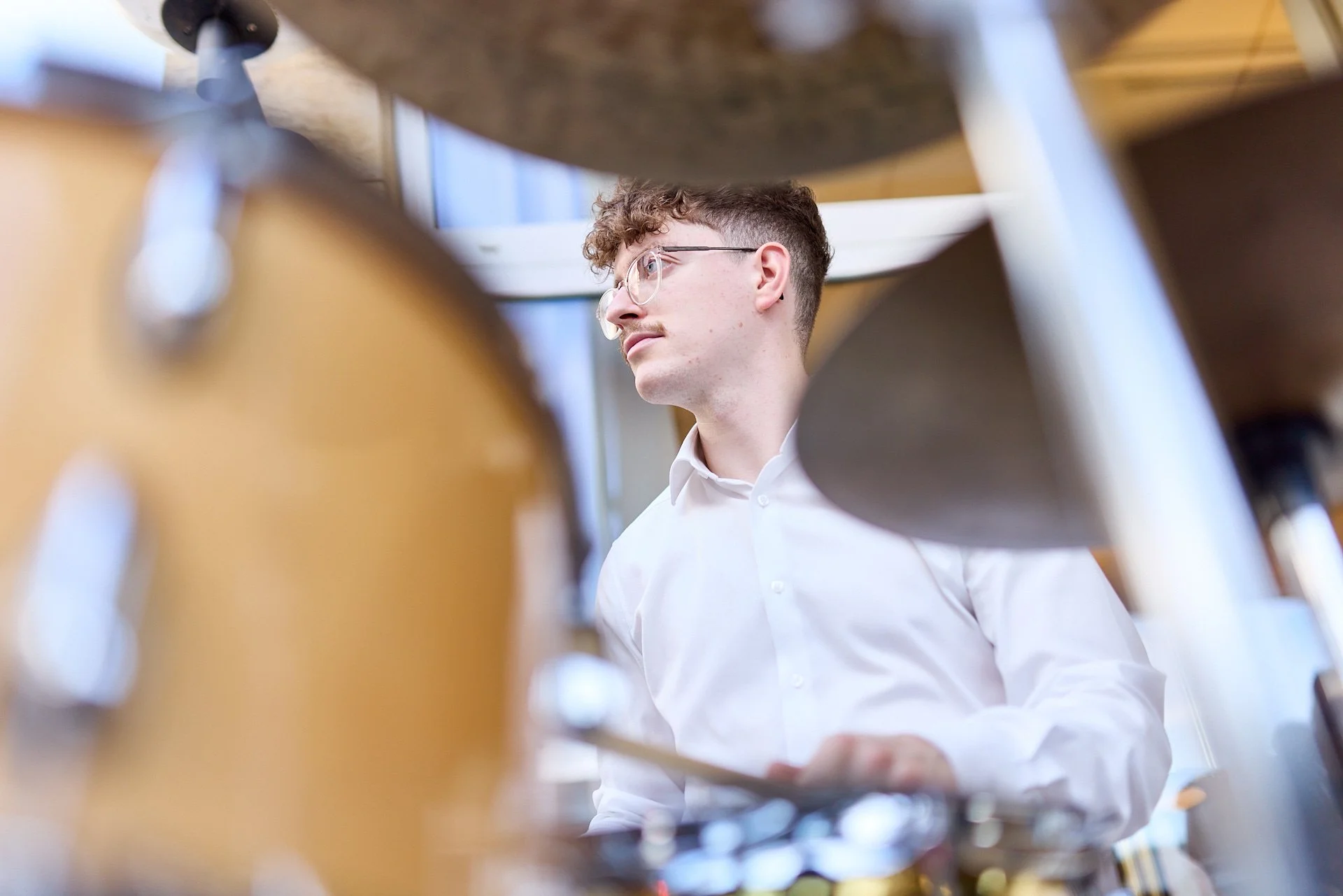 Junge Mann in weißem Hemd, betrachtet durch eine Gruppe von Musikinstrumenten.