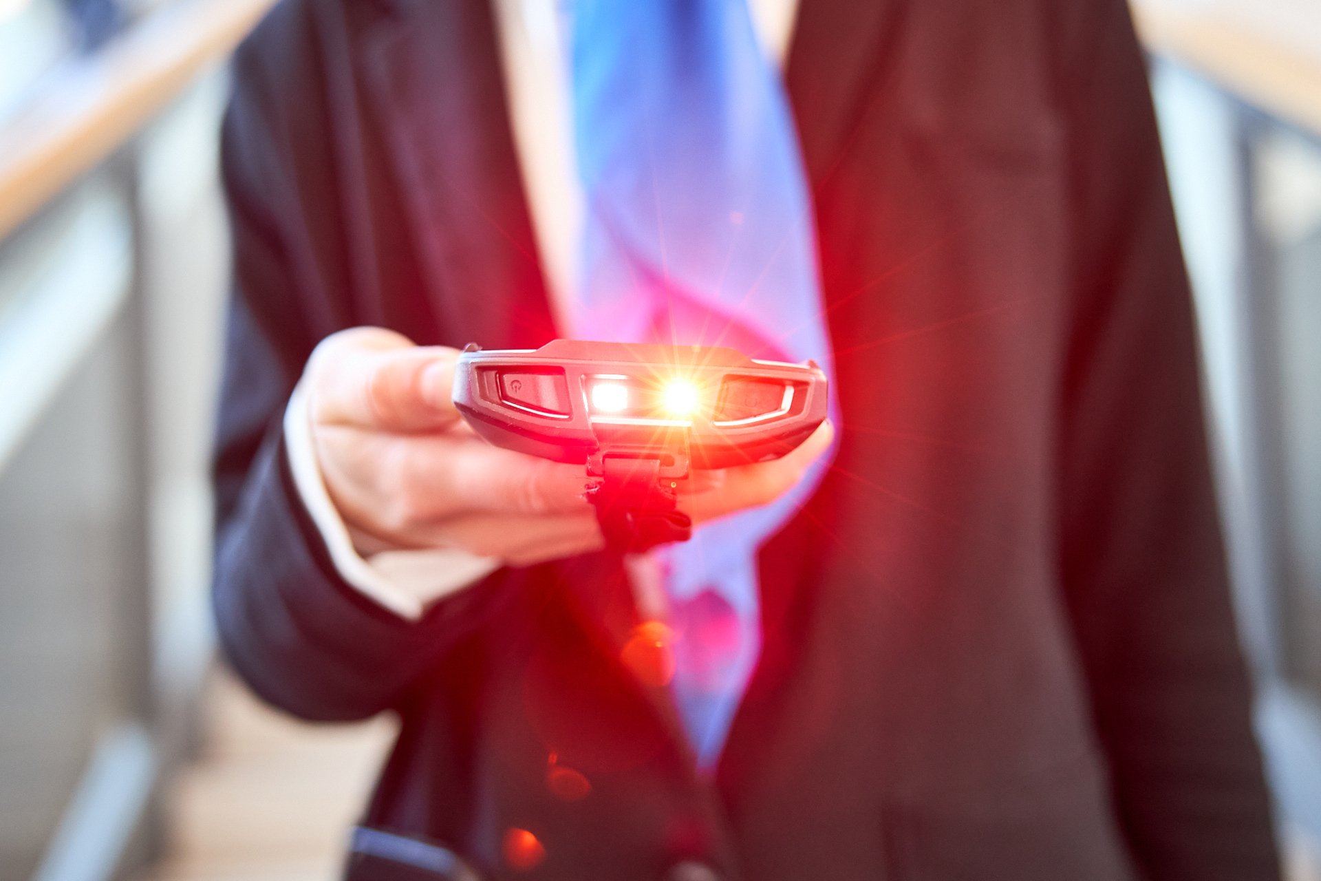 Eine Person in einem dunklen Anzug hält ein Smartphone, auf dem ein rotes Laserlicht projiziert wird.