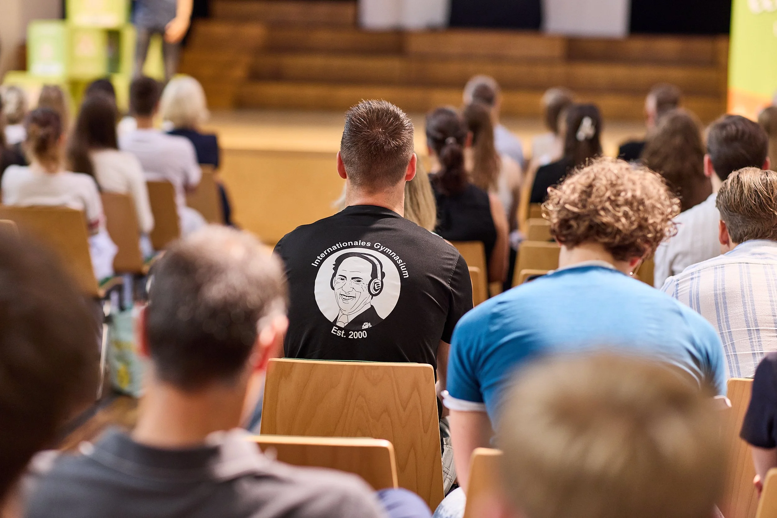 Menschen sitzen in einem Hörsaal bei einer Veranstaltung, der Blick ist auf die Bühne gerichtet.