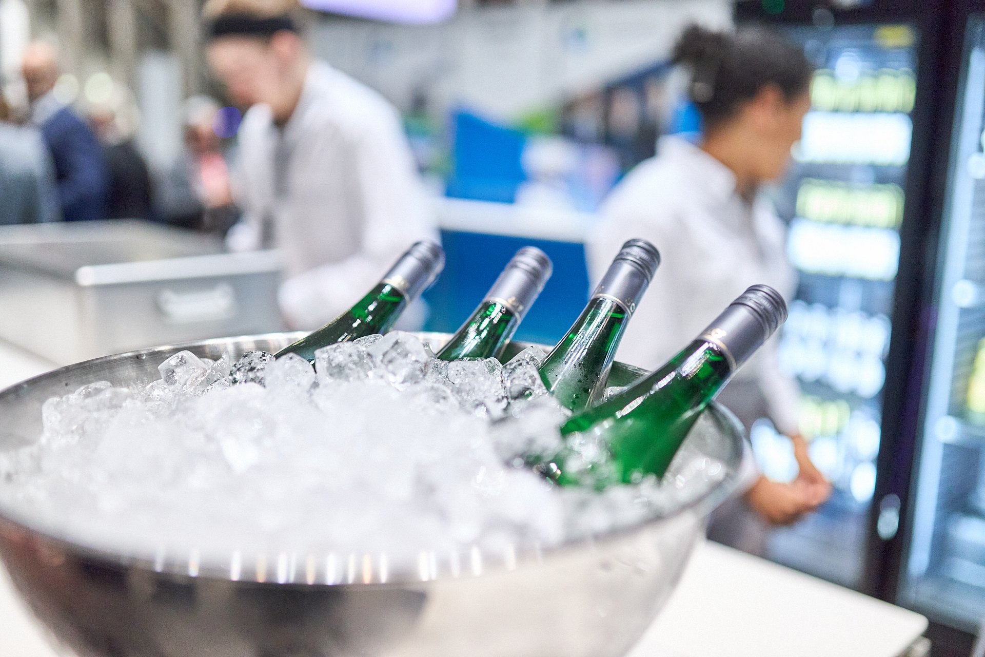 Grüne Flaschen in einer Eistruhe, im Hintergrund zwei Köche in einer Küche