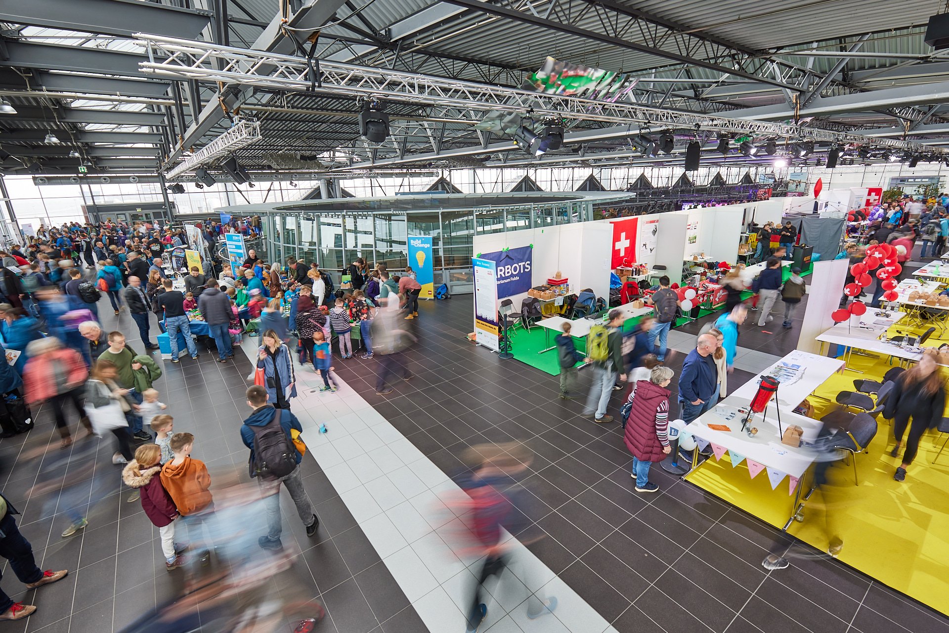Verschiedene Messestände und viele Besucher in einer großen Halle bei einer Messe oder Veranstaltung.