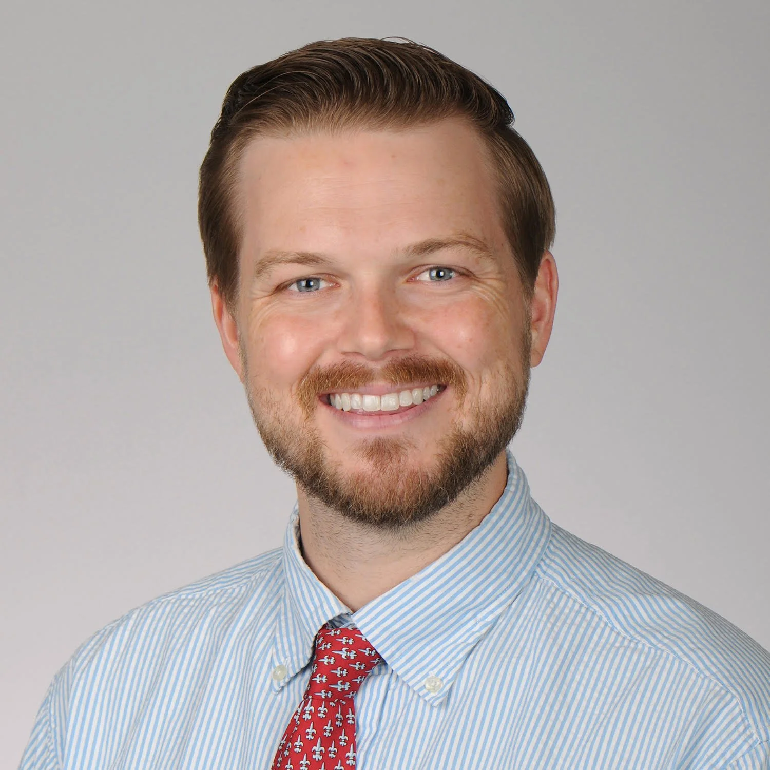Person wearing a cap and sunglasses, holding a mug, standing outdoors with a grassy background.