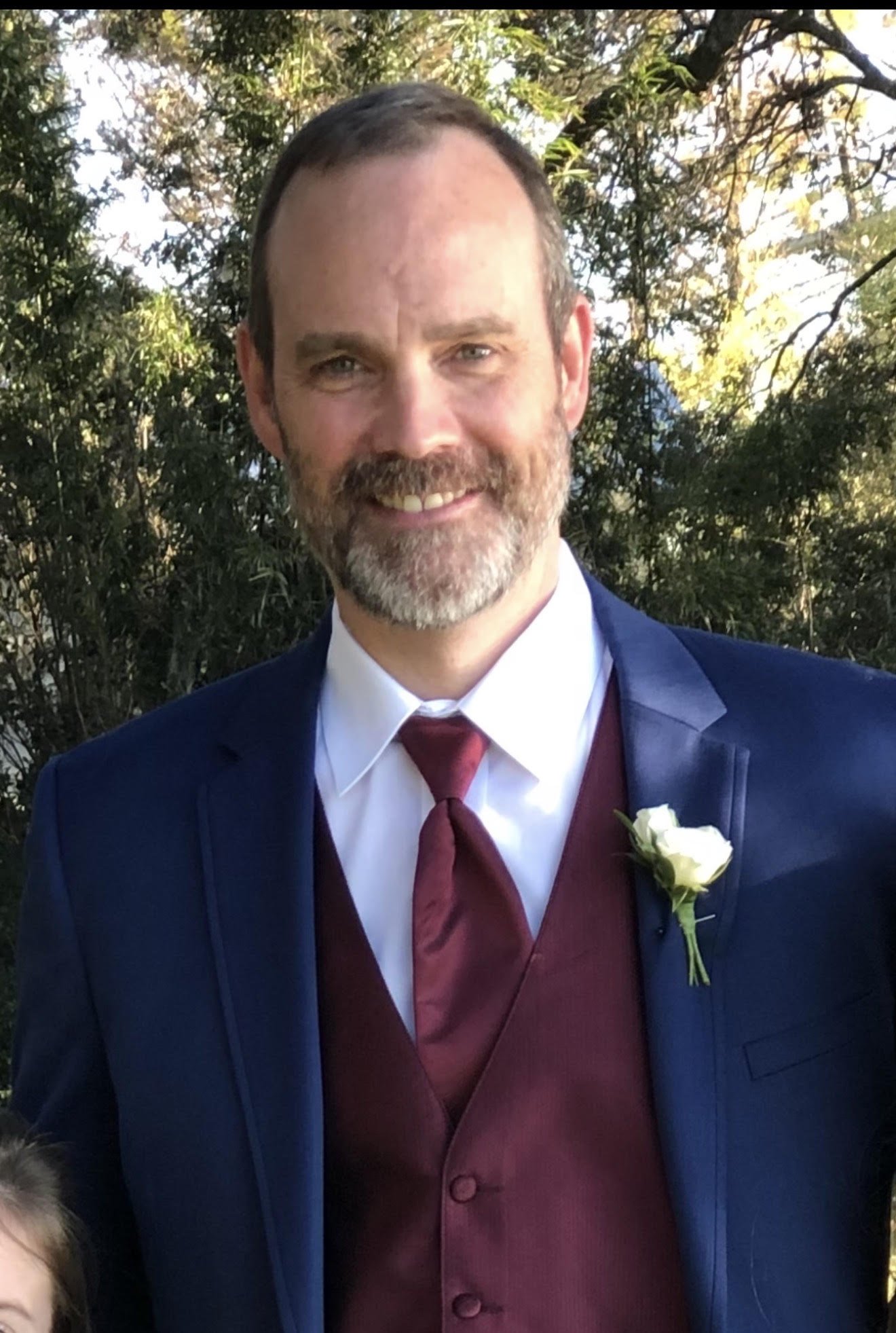 A man in a suit and tie smiling, with a dark gray background.