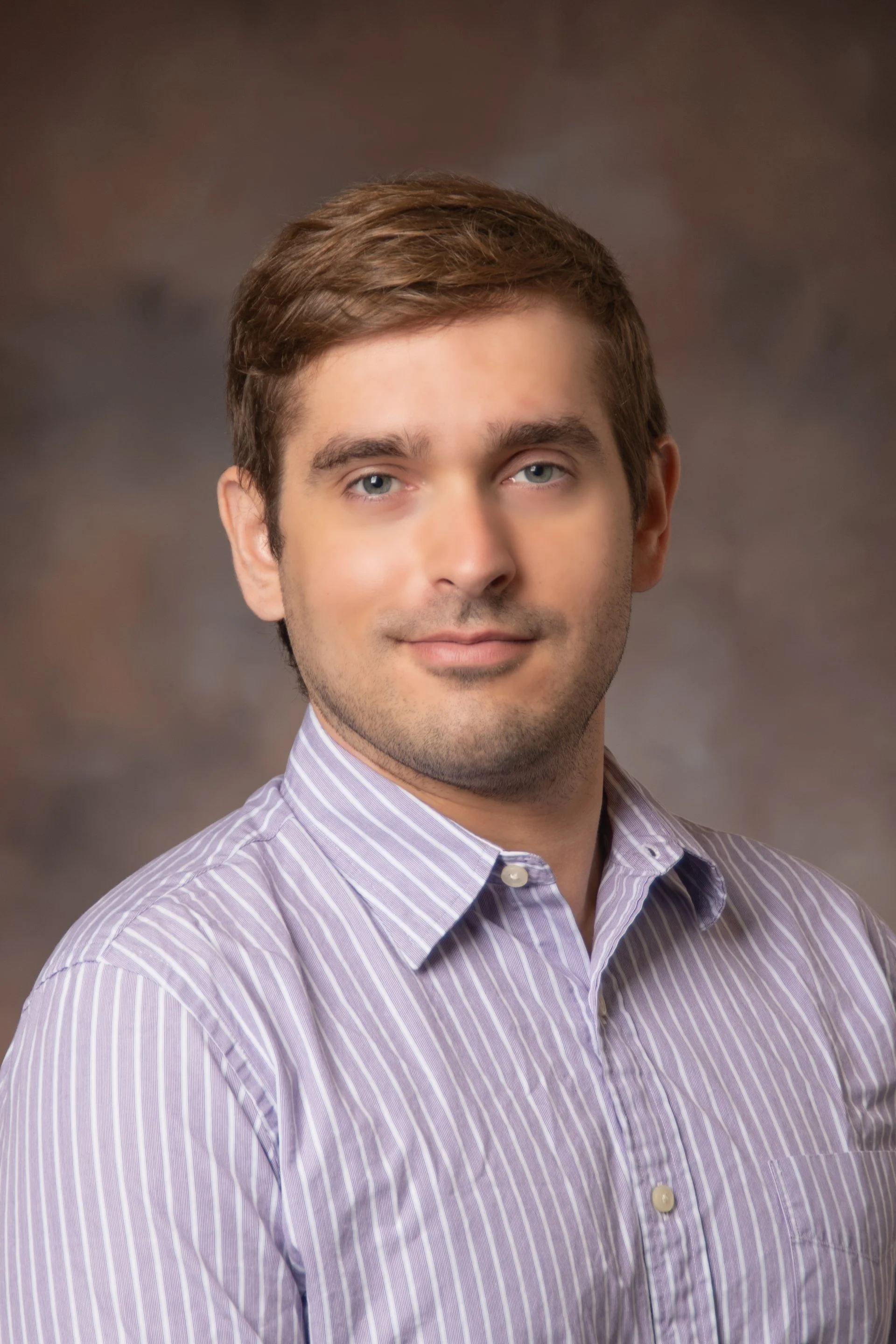 Person wearing sunglasses smiling outdoors with trees in the background