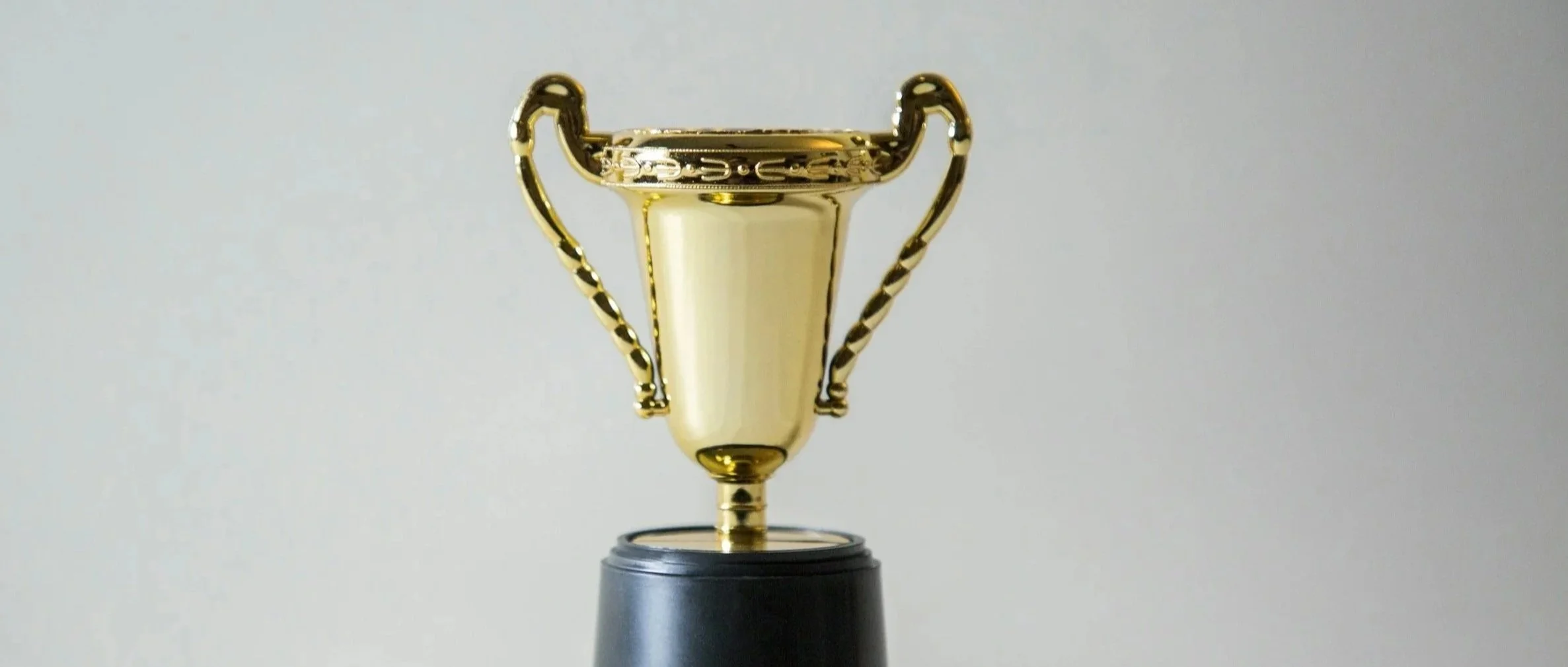 A gold trophy cup with black base on a plain light background.