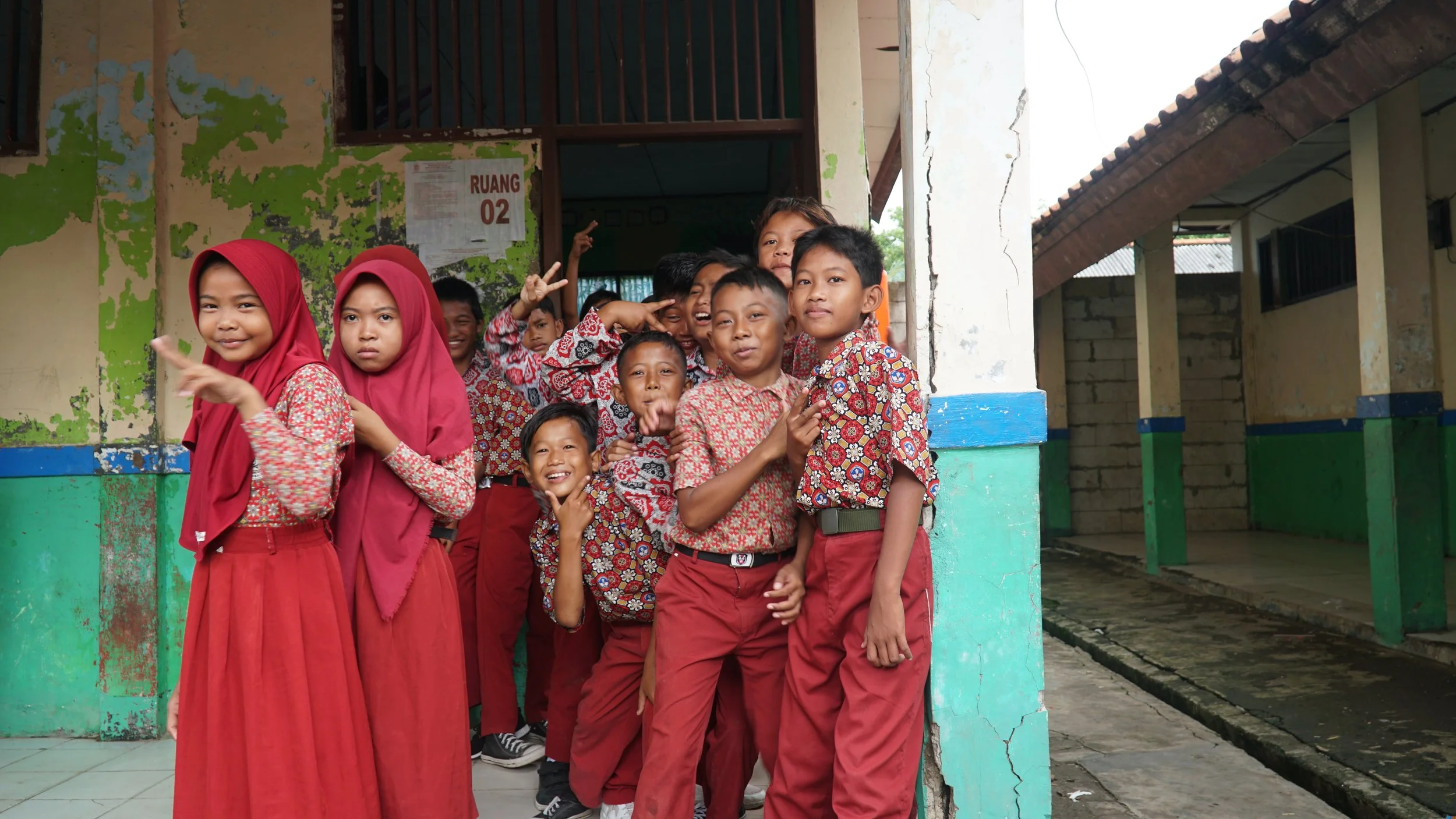 Group of schoolchildren in uniform standing outside a classroom in Indonesia, smiling and posing playfully.
