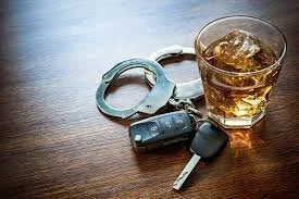 A glass of whiskey, a car key, and a pair of handcuffs on a wooden table. Jacob Fisher is the attorney to call!