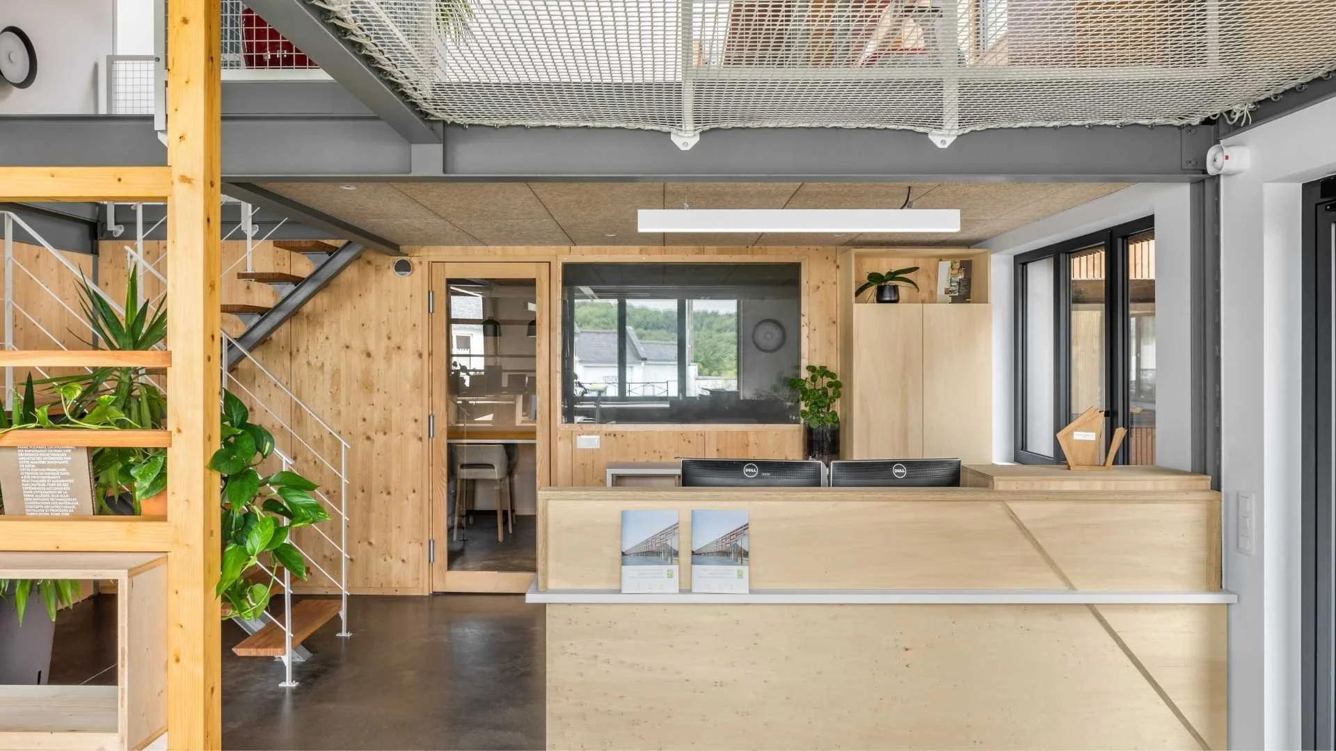Accueil mobilier sur mesure en bois au sein d'un bureau à l'esprit loft industriel. Escalier et garde-corps en métal, mezzanine en filet de catamaran pour le repos des employés à l'heure du déjeuner