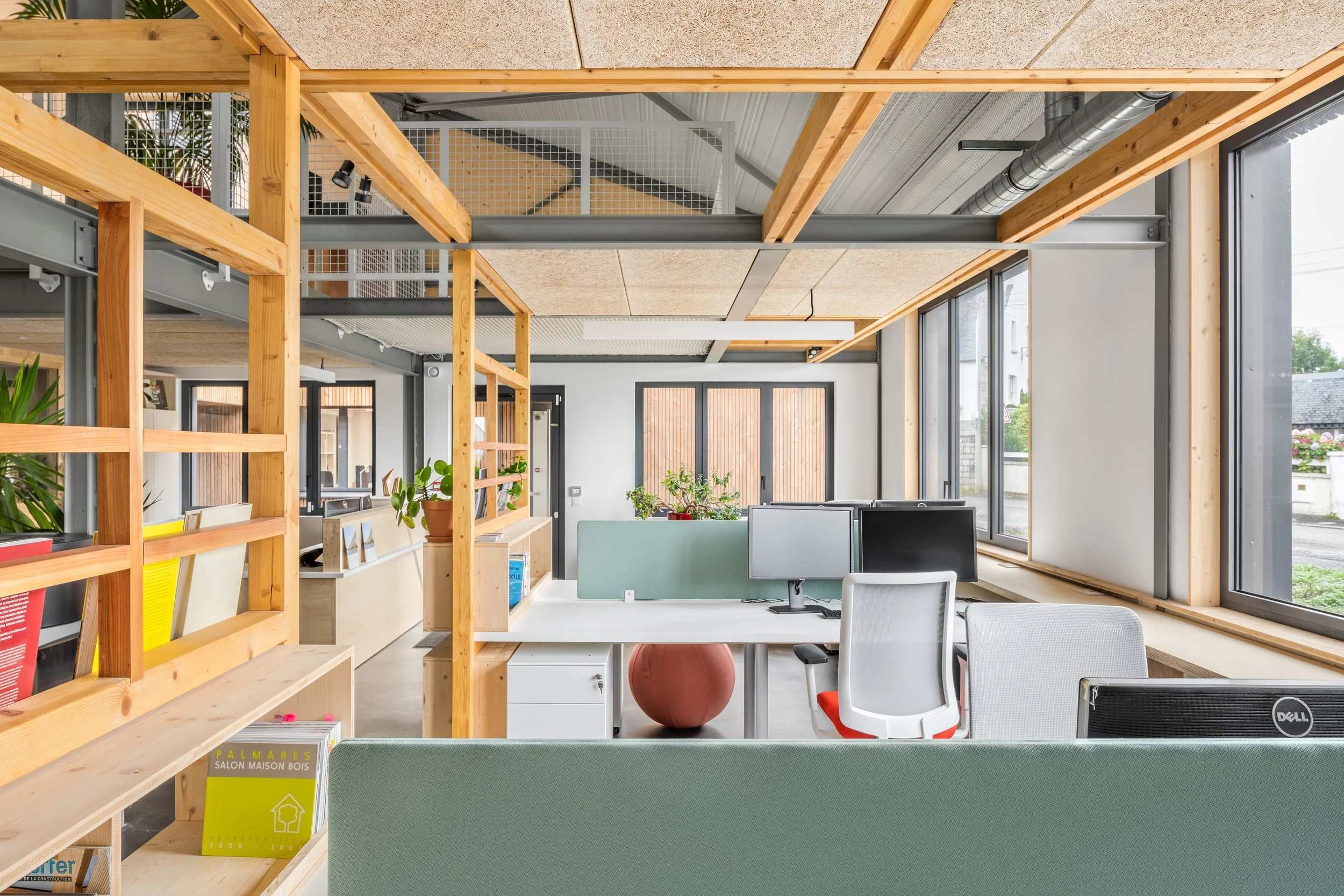 Intérieur d'un bureau avec mobilier moderne, bureaux équipés d'ordinateurs, grandes fenêtres laissant entrer la lumière naturelle, éléments en bois et en métal, plantes décoratives, ambiance lumineuse et ouverte.